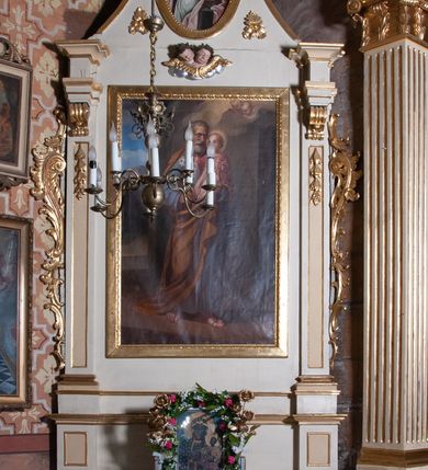 Zdjęcie nr 3: Ołtarz architektoniczny, jednoosiowy, jednokondygnacyjny ze zwieńczeniem, z uszami. Retabulum ustawione na prostopadłościennej mensie ołtarzowej z antepedium, zdobionym czterema prostokątnymi płycinami oddzielonymi kanelowanymi lizenami. Tabernakulum w kształcie prostopadłościennej skrzynki na wysokim cokole, zamkniętej od góry płaskim daszkiem, na którym miejsce na prosty tron do wystawiania monstrancji. Przednia ścianka tabernakulum zamknięta od góry gzymsem w formie łuku nadwieszonego. Drzwiczki w formie stojącego prostokąta zamkniętego łukiem półkolistym. W polu, obwiedzionym ramą o analogicznym kształcie płaskorzeźbiony krzyż z podstawą. Ustawiona na mensie nastawa wsparta na cokole z wyodrębnionymi po bokach dwoma postumentami, wyżej ujęta parą pilastrów, o trzonach ozdobionych płycinami i u góry zwisami ze stylizowanych kampanul, z nałożonymi u szczytu konsolkami pełniącymi funkcję kapiteli, które wspierają odcinki przerwanego belkowania. W polu głównym obraz św. Józefa z Dzieciątkiem Jezus w kształcie pionowego prostokąta. Zwieńczenie  w ogólnym zarysie w kształcie trapezu, o bokach zaakcentowanych wklęsłymi łukami odcinkowymi, zamknięte od góry dwiema wolutkami, spiętymi u szczytu muszlą palmetową i ozdobionymi wicią z różami. W polu owalny obraz z przedstawieniem św. Wiktorii. Poniżej dwie uskrzydlone główki aniołków. Uszy z wici i motywów ornamentu rocaille'owego. Struktura ołtarza w kolorze białym, detale i ornamentyka złocone.