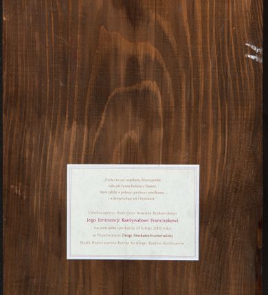 Zdjęcie nr 2: Obraz w formie stojącego prostokąta. W centrum przedstawienie popiersia Marii i Jezusa ukazanego jako dziecko, zwróconych w trzech czwartych w lewo, z pochylonymi głowami. Twarz Marii pociągła, o dużych, migdałowatych oczach, łukowatych brwiach, prostym, wąskim nosie i małych ustach. Ubrana jest w czerwoną suknię oraz brązowy płaszcz o niebieskiej lamówce zarzucony na głowę i ramiona. Przed Marią znajduje się mniejsza postać Jezusa. Jego twarz jest pociągła, o dużych, migdałowatych oczach, łukowatych brwiach, wąskim nosie i małych ustach, okolona krótkimi, brązowymi włosami. Ubrany jest ciemnobrązową tunikę, o wzorze w pasy. Wokół głów Marii i Jezusa złocone nimby. Postacie ukazane na niebieskim tle. Miedzy Marią a Jezusem napis: „HAY / QUE HACER / [...]DADIS / CAISTIANAS / COMO LA / SAGRADA FALIMIA / DE NAZARET”. Obok głowy Jezusa napis: „QUE / VIVA/EN / HUMIL/DAD / SENCILLE / YALABAN/ZIA / [...]”. W górnych narożach obrazu napisy: „MARIA” i „[...] / 1973”. Na odwrocie obrazu przyklejona drukowana kartka z napisem: „«Trzeba tworzyć wspólnoty chrześcijańskie, / takie jak Święta Rodzina z Nazaret, / które żyłyby w pokorze, prostocie i uwielbieniu, / i w których drugi jest Chrystusem.» / Umiłowanemu Pasterzowi Kościoła Krakowskiego / Jego Eminencji Kardynałowi Franciszkowi / na pamiątkę spotkania 18 lutego 2002 roku / ze Wspólnotami Drogi Neokatechumenalnej / Parafii Podwyższenia Krzyża Świętego, Kraków-Kurdwanów”. 