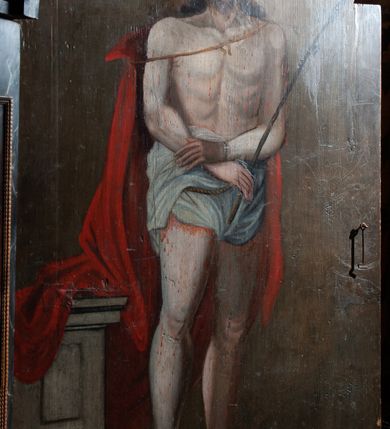 Zdjęcie nr 3: Obraz w kształcie stojącego prostokąta zamkniętego łukiem półkolistym. W centrum kompozycji przedstawiony Chrystus w typie Ecce Homo. Postać ukazana w pozycji stojącej, frontalnie z głową zwróconą nieznacznie w prawo. Ręce skrzyżowane na wysokości bioder, w prawej dłoni trzyma trzcinę. Chrystus przedstawiony jako młody mężczyzna o pociągłej twarzy, długich brązowych włosach i krótkim zaroście. Wzrok skierowany w dół. Na głowie Zbawiciela umieszczona cierniowa korona, a wokół niej świetlisty nimb. Tors nagi, wokół bioder udrapowane białe perizonium, na ramiona luźno narzucony czerwony płaszcz. Na drugim planie, z lewej strony kompozycji ukazany kamienny postument zwieńczony profilowanym gzymsem. Tło jednolite, ciemnobrązowe. 