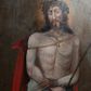 Zdjęcie nr 1: Obraz w kształcie stojącego prostokąta zamkniętego łukiem półkolistym. W centrum kompozycji przedstawiony Chrystus w typie Ecce Homo. Postać ukazana w pozycji stojącej, frontalnie z głową zwróconą nieznacznie w prawo. Ręce skrzyżowane na wysokości bioder, w prawej dłoni trzyma trzcinę. Chrystus przedstawiony jako młody mężczyzna o pociągłej twarzy, długich brązowych włosach i krótkim zaroście. Wzrok skierowany w dół. Na głowie Zbawiciela umieszczona cierniowa korona, a wokół niej świetlisty nimb. Tors nagi, wokół bioder udrapowane białe perizonium, na ramiona luźno narzucony czerwony płaszcz. Na drugim planie, z lewej strony kompozycji ukazany kamienny postument zwieńczony profilowanym gzymsem. Tło jednolite, ciemnobrązowe. 