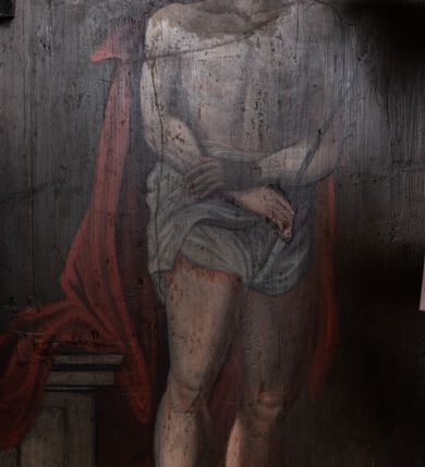 Zdjęcie nr 5: Obraz w kształcie stojącego prostokąta zamkniętego łukiem półkolistym. W centrum kompozycji przedstawiony Chrystus w typie Ecce Homo. Postać ukazana w pozycji stojącej, frontalnie z głową zwróconą nieznacznie w prawo. Ręce skrzyżowane na wysokości bioder, w prawej dłoni trzyma trzcinę. Chrystus przedstawiony jako młody mężczyzna o pociągłej twarzy, długich brązowych włosach i krótkim zaroście. Wzrok skierowany w dół. Na głowie Zbawiciela umieszczona cierniowa korona, a wokół niej świetlisty nimb. Tors nagi, wokół bioder udrapowane białe perizonium, na ramiona luźno narzucony czerwony płaszcz. Na drugim planie, z lewej strony kompozycji ukazany kamienny postument zwieńczony profilowanym gzymsem. Tło jednolite, ciemnobrązowe. 