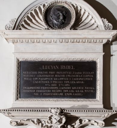 Zdjęcie nr 1: Epitafium w formie leżącego prostokąta, wsparte na szerokim, wydatnym gzymsie z perełkowaniem, z narożami ujętymi liśćmi, z konsolą z wolutami i liśćmi oraz uskrzydloną główką anioła oraz owalnym herbem Uniwersytetu Jagiellońskiego w ozdobnym kartuszu, zwieńczonym koroną. Tablicę wieńczy gzyms z motywem wolich oczu, na którym osadzone jest półkoliste zwieńczenie z akroterionami, wypełnione muszlą palmetową i okrągłym medalionem obwiedzionym motywem wolich oczu z płaskorzeźbionym wizerunkiem zmarłego. Postać ukazana jest w popiersiu, zwrócona w lewo, o twarzy wyrazistej, z wąsami i wysokim czołem z zakolami. W marmurowej tablicy inskrypcja: „LUCYAN RYDEL / MED(YCYNY) I CHIR(URGII): DOKTOR PROF(ESOR) OKULISTYKI, 3 krotnie DZIEKAN / WYDZIAŁU LEKARSKIEGO, REKTOR UNI(WERSYTETU) JAGIEL(LOŃSKIEGO) CZŁONEK / WIELU TOW(ARZYSTW) NAUKOWYCH KRAJOWYCH I ZAGRANICZNYCH / ZAŁOŻYCIEL I PREZES TOW(ARZYSTWA) LEK(ARSKIEGO) KRAK(OWSKIEGO) / *17/10 1833 †27/4 1895 / ZNAKOMITEMU PROFESOROWI, ZACNEMU KOLEDZE, NIESKA/ZITELNEGO CHARAKTERU MĘŻOWI, TOW(ARZYSTWO) LEK(ARSKIE) KRAK(OWSKIE) WSPOL/NIE Z PROFESORAMI UNIW(ERSYTETU) JAGIEL(LOŃSKIEGO)”. Na medalionie sygnatura: „Z[ygmunt] Langman / Kraków”.