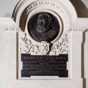 Zdjęcie nr 1: Epitafium zbliżone do kwadratu, w kamiennej, szerokiej ramie, z uszakami, zwieńczone gzymsem w formie nadwieszonego łuku, profilowanym, z motywem wolich oczu, zwieńczonym krzyżem na tle muszli palmetowej. Dolna część ramy ze spływami wolutowymi podtrzymującymi uskrzydloną główkę anioła, ujęta łezkami. W części środkowej owalny medalion z płaskorzeźbionym popiersiem zmarłego, ujętego w trzech czwartych, zwróconego w prawo, o realistyczne oddanej twarzy, z długim nosem, brodą i włosami zaczesanymi do tyłu. Pod medalionem gałązki lauru i dębu z żołędziami z karbowaną wstęgą i herb Uniwersytetu Jagiellońskiego w kartuszu. W dolnej części prostokątna tablica z dębnickiego marmuru z uszkami, w polu której inskrypcja: „MAURYCEMU FIERICHOWI / *12/V 1856. † 29/VI 1889. / D(OKTO)ROWI O(BOJGA) PRAW ZWYCZAJ(AJNEMU) PROF(ESOROWI) UNIW(ERSYTETU) JAGIEL(LOŃSKIEGO) / MĘŻOWI, / KTÓRY POZOSTAWIWSZY WIELE ŚWIATŁA W NAUCE, / PRZEDWCZEŚNIE ZASNĄŁ W PANU. / PRAWDZIWEMU PRZYJACIELOWI MŁODZIEŻY / AKADEMICKIEJ. / NAJLEPSZEMU SYNOWI I BRATU / W NIEUTULONYM ŻALU RODZINA”. Na medalionie kuta sygnatura: „T(adeusz) Błotnicki / 1891”.