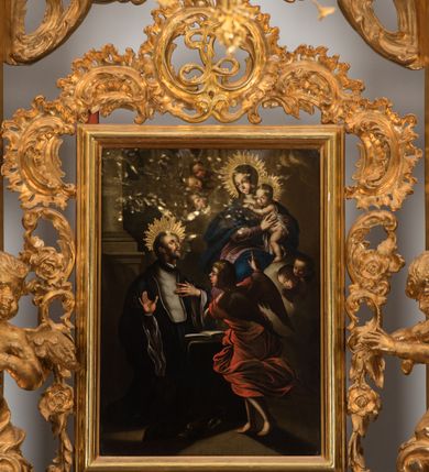 Zdjęcie nr 3: Na brązowym tle, z kolumną w lewej części kompozycji i lekko rozjaśnionymi obłokami, ukazany św. Jan Kanty klęczący przed siedzącą w chmurach Matką Boską z Dzieciątkiem i stojącym przed klęcznikiem aniołem. Święty spoczywa na klęczniku z otwartą księgą, ukazany jest w trzech czwartych, zwrócony w swoją lewą stronę, lewą ręką złożoną na piersi, a z prawą lekko uniesioną, z otwartą dłonią skierowaną w stronę Matki Boskiej. Jego twarz jest pociągła, oczy wydatne, uniesione w kierunku Marii. Jego nos jest długi, czoło wysokie, głowa okolona krótkimi, brązowymi włosami, a twarz krótką brodą z krótkimi wąsami. Wokół głowy aplikowana gloria z promieni o zróżnicowanej długości. Święty jest ubrany w długą uniwersytecką togę z białym plastronem. Maria ukazana frontalnie, w pozycji siedzącej, trzyma na kolanach stojące Dzieciątko. Jej twarz jest łagodna, oczy migdałowate, nos wydatny, usta drobne, włosy długie, brązowe, opadające na plecy. Ubrana w różową suknię i niebieski płaszcz okrywający ramiona i kolana. Jezus przedstawiony jest w trzech czwartych, niemal nagi, okryty z przodu i tyłu białą tkaniną, o twarzy okrągłej, z krótkimi włosami i pulchnej dziecięcej sylwecie. Nad głowami Marii i Jezusa utworzone ze złoconych promieni korony. Przed świętym stoi anioł, ukazany niemalże od tyłu, w pozycji stojącej, z lekko zgiętą lewą nogą. Ubrany jest w czerwoną, rozwianą, drobno marszczoną suknię, z głową zwróconą w kierunku świętego, z prawą ręką uniesioną, wskazuje palcem na Matkę Boską z Dzieciątkiem. Z obu stron Matki Boskiej uskrzydlone głowy aniołów wyłaniające się z obłoków. Obraz utrzymany w ciemnej tonacji kolorystycznej, z silnymi rozświetlonymi akcentami brązów, czerni, czerwieni i błękitów. Na odwrocie blachy wyryta inskrypcja: „Poninski 1778”. 