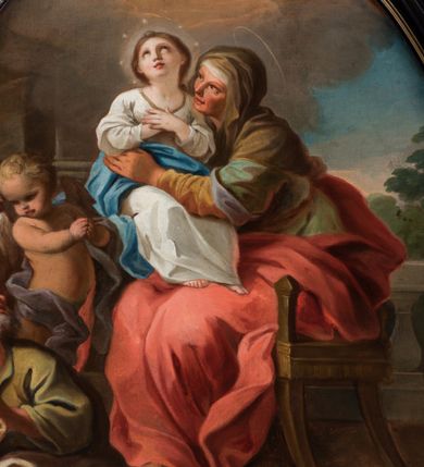 Zdjęcie nr 3: Kompozycja owalna w drewnianej, czarnej, profilowanej ramie, ukazuje siedzącą na krześle św. Annę z młodą Marią na jej kolanach i św. Joachima siedzącego u jej stóp z parą stojących za nim aniołów. Święta Anna ukazana jest w trzech czwartych, jej twarz jest wyrazista, oddana szkicowo, nos mały, usta uśmiechnięte, oczy zwrócone ku Marii. Ubrana jest w zielono-brązową suknię, czerwony płaszcz i brązową chustę zarzuconą na głowę. Maria przedstawiona jest frontalnie z rękami złożonymi na piersi, w białej sukni z brązową lamówka i niebieskim płaszczu okalającym biodra. Jej twarz jest okrągła, oczy uniesione ku górze, nos szeroki a usta wąskie; wokół głowy zarysowana jasna poświata z wieńcem z gwiazd. Święty Joachim został ukazany frontalnie, z głową odchyloną w kierunku św. Anny, ubrany w zieloną suknię i biały płaszcz; w ręku trzyma księgę w brązowej oprawie. Jego twarz ukazana wyraziście, z siwymi, skręconymi włosami i siwą, krótką, kręconą brodą. Za nim stoją dwa nagie putta, z tkaninami wokół bioder. W tle balustrada z lalkami, za którą widoczny krzew i lazurowe niebo oraz skłębione chmury, rozświetlone wokół hebrajskiej imienia Marii („מרים”).