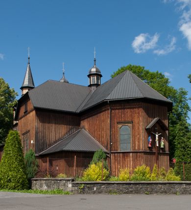 Zdjęcie nr 4: Kościół drewniany, o konstrukcji ramowej, na kamiennej podmurówce, elewacje jednolite, szalowane z listwowaniem o układzie pionowym z gzymsami pseudoarkadkowymi. Wieża zachodnia o konstrukcji słupowej, z szalunkiem o układzie poziomym z fryzem arkadkowym w górnej partii. Więźba dachowa drewniana, krokwiowa. Budynek na betonowym podmurowaniu przesłoniętym daszkiem gontowym. Kościół orientowany, trójnawowy, na rzucie wydłużonego krzyża, z płytkim transeptem, prezbiterium zakończone trójbocznie, z zakrystią przylegającą od południa, na skrzyżowaniu naw kopuła. Od zachodu wieża czterokondygnacyjna, na planie kwadratu przechodzącego w kwadrat o coraz bardziej ściętych narożach, ujęta dwiema kruchtami na rzucie kwadratu. Wnętrze o układzie bazylikowym, nawy podzielone smukłymi, żeliwnymi kolumienkami. Pomiędzy nawą a prezbiterium otwór tęczowy w formie kwadratu o ściętych narożach. Parapet chóru muzycznego w zachodniej części kościoła podparty na czterech kolumienkach. Nawa główna nakryta stropem z widocznymi elementami konstrukcji więźby, nawy boczne przekryte pułapami deskowymi. Posadzka z płyt kamiennych. Elewacja frontowa w formie wieży z dwoma kruchtami. Na każdej z trzech osi wejście z dwuskrzydłowymi drzwiami klepkowymi o układzie rombowym, z oknami w partii szczytu, nakryte daszkami okapowymi. Nad wejściem głównym żeliwna tabliczka z napisem „E(RZ)H(ERZOG) / ALBRECHT / 1888”. Na każdej kondygnacji wieży okna w formie stojącego prostokąta zwieńczone daszkami pulpitowymi, na pierwszej jedno, na drugiej trzy, na trzeciej cztery, na czwartej osiem. W elewacji północnej i południowej cztery podwójne otwory okienne w formie stojącego prostokąta o ściętych górnych narożach w partii naw bocznych oraz pięć okienek w formie leżącego prostokąta w partii nawy głównej. W elewacji południowej wejście z dwuskrzydłowymi drzwiami klepkowymi o układzie rombowym. Na osi skrzydeł transeptu po jednym otworze okiennym w formie stojącego prostokąta o ściętych górnych narożach. Na ścianie wschodniej prezbiterium Ogrójec w formie grupy Ukrzyżowania nakrytej daszkiem pulpitowym, flankowany dwoma otworami okiennymi w kształcie stojącego prostokąta o ściętych górnych narożach. Nawa główna nakryta dachem dwuspadowym. W połowie długości dachu oraz na skrzyżowaniu naw wznoszą się ponad kalenicą wieżyczki na sygnaturkę, na ośmiobocznym obitym blachą trzonie, z latarniami zwieńczonymi cebulastymi hełmami. Nad nawami bocznymi dachy pulpitowe, ramiona transeptu nakrywają dachy naczółkowe. Wieża zwieńczona dachem wieżowym, ośmiobocznym, z iglicą zakończoną krzyżem. 


