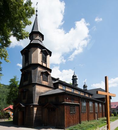 Zdjęcie nr 3: Kościół drewniany, o konstrukcji ramowej, na kamiennej podmurówce, elewacje jednolite, szalowane z listwowaniem o układzie pionowym z gzymsami pseudoarkadkowymi. Wieża zachodnia o konstrukcji słupowej, z szalunkiem o układzie poziomym z fryzem arkadkowym w górnej partii. Więźba dachowa drewniana, krokwiowa. Budynek na betonowym podmurowaniu przesłoniętym daszkiem gontowym. Kościół orientowany, trójnawowy, na rzucie wydłużonego krzyża, z płytkim transeptem, prezbiterium zakończone trójbocznie, z zakrystią przylegającą od południa, na skrzyżowaniu naw kopuła. Od zachodu wieża czterokondygnacyjna, na planie kwadratu przechodzącego w kwadrat o coraz bardziej ściętych narożach, ujęta dwiema kruchtami na rzucie kwadratu. Wnętrze o układzie bazylikowym, nawy podzielone smukłymi, żeliwnymi kolumienkami. Pomiędzy nawą a prezbiterium otwór tęczowy w formie kwadratu o ściętych narożach. Parapet chóru muzycznego w zachodniej części kościoła podparty na czterech kolumienkach. Nawa główna nakryta stropem z widocznymi elementami konstrukcji więźby, nawy boczne przekryte pułapami deskowymi. Posadzka z płyt kamiennych. Elewacja frontowa w formie wieży z dwoma kruchtami. Na każdej z trzech osi wejście z dwuskrzydłowymi drzwiami klepkowymi o układzie rombowym, z oknami w partii szczytu, nakryte daszkami okapowymi. Nad wejściem głównym żeliwna tabliczka z napisem „E(RZ)H(ERZOG) / ALBRECHT / 1888”. Na każdej kondygnacji wieży okna w formie stojącego prostokąta zwieńczone daszkami pulpitowymi, na pierwszej jedno, na drugiej trzy, na trzeciej cztery, na czwartej osiem. W elewacji północnej i południowej cztery podwójne otwory okienne w formie stojącego prostokąta o ściętych górnych narożach w partii naw bocznych oraz pięć okienek w formie leżącego prostokąta w partii nawy głównej. W elewacji południowej wejście z dwuskrzydłowymi drzwiami klepkowymi o układzie rombowym. Na osi skrzydeł transeptu po jednym otworze okiennym w formie stojącego prostokąta o ściętych górnych narożach. Na ścianie wschodniej prezbiterium Ogrójec w formie grupy Ukrzyżowania nakrytej daszkiem pulpitowym, flankowany dwoma otworami okiennymi w kształcie stojącego prostokąta o ściętych górnych narożach. Nawa główna nakryta dachem dwuspadowym. W połowie długości dachu oraz na skrzyżowaniu naw wznoszą się ponad kalenicą wieżyczki na sygnaturkę, na ośmiobocznym obitym blachą trzonie, z latarniami zwieńczonymi cebulastymi hełmami. Nad nawami bocznymi dachy pulpitowe, ramiona transeptu nakrywają dachy naczółkowe. Wieża zwieńczona dachem wieżowym, ośmiobocznym, z iglicą zakończoną krzyżem. 


