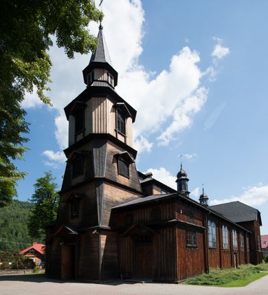 Zdjęcie nr 2: Kościół drewniany, o konstrukcji ramowej, na kamiennej podmurówce, elewacje jednolite, szalowane z listwowaniem o układzie pionowym z gzymsami pseudoarkadkowymi. Wieża zachodnia o konstrukcji słupowej, z szalunkiem o układzie poziomym z fryzem arkadkowym w górnej partii. Więźba dachowa drewniana, krokwiowa. Budynek na betonowym podmurowaniu przesłoniętym daszkiem gontowym. Kościół orientowany, trójnawowy, na rzucie wydłużonego krzyża, z płytkim transeptem, prezbiterium zakończone trójbocznie, z zakrystią przylegającą od południa, na skrzyżowaniu naw kopuła. Od zachodu wieża czterokondygnacyjna, na planie kwadratu przechodzącego w kwadrat o coraz bardziej ściętych narożach, ujęta dwiema kruchtami na rzucie kwadratu. Wnętrze o układzie bazylikowym, nawy podzielone smukłymi, żeliwnymi kolumienkami. Pomiędzy nawą a prezbiterium otwór tęczowy w formie kwadratu o ściętych narożach. Parapet chóru muzycznego w zachodniej części kościoła podparty na czterech kolumienkach. Nawa główna nakryta stropem z widocznymi elementami konstrukcji więźby, nawy boczne przekryte pułapami deskowymi. Posadzka z płyt kamiennych. Elewacja frontowa w formie wieży z dwoma kruchtami. Na każdej z trzech osi wejście z dwuskrzydłowymi drzwiami klepkowymi o układzie rombowym, z oknami w partii szczytu, nakryte daszkami okapowymi. Nad wejściem głównym żeliwna tabliczka z napisem „E(RZ)H(ERZOG) / ALBRECHT / 1888”. Na każdej kondygnacji wieży okna w formie stojącego prostokąta zwieńczone daszkami pulpitowymi, na pierwszej jedno, na drugiej trzy, na trzeciej cztery, na czwartej osiem. W elewacji północnej i południowej cztery podwójne otwory okienne w formie stojącego prostokąta o ściętych górnych narożach w partii naw bocznych oraz pięć okienek w formie leżącego prostokąta w partii nawy głównej. W elewacji południowej wejście z dwuskrzydłowymi drzwiami klepkowymi o układzie rombowym. Na osi skrzydeł transeptu po jednym otworze okiennym w formie stojącego prostokąta o ściętych górnych narożach. Na ścianie wschodniej prezbiterium Ogrójec w formie grupy Ukrzyżowania nakrytej daszkiem pulpitowym, flankowany dwoma otworami okiennymi w kształcie stojącego prostokąta o ściętych górnych narożach. Nawa główna nakryta dachem dwuspadowym. W połowie długości dachu oraz na skrzyżowaniu naw wznoszą się ponad kalenicą wieżyczki na sygnaturkę, na ośmiobocznym obitym blachą trzonie, z latarniami zwieńczonymi cebulastymi hełmami. Nad nawami bocznymi dachy pulpitowe, ramiona transeptu nakrywają dachy naczółkowe. Wieża zwieńczona dachem wieżowym, ośmiobocznym, z iglicą zakończoną krzyżem. 


