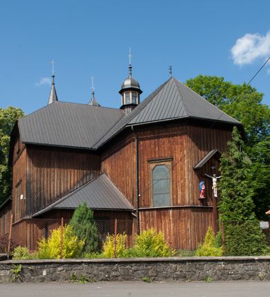 Zdjęcie nr 5: Kościół drewniany, o konstrukcji ramowej, na kamiennej podmurówce, elewacje jednolite, szalowane z listwowaniem o układzie pionowym z gzymsami pseudoarkadkowymi. Wieża zachodnia o konstrukcji słupowej, z szalunkiem o układzie poziomym z fryzem arkadkowym w górnej partii. Więźba dachowa drewniana, krokwiowa. Budynek na betonowym podmurowaniu przesłoniętym daszkiem gontowym. Kościół orientowany, trójnawowy, na rzucie wydłużonego krzyża, z płytkim transeptem, prezbiterium zakończone trójbocznie, z zakrystią przylegającą od południa, na skrzyżowaniu naw kopuła. Od zachodu wieża czterokondygnacyjna, na planie kwadratu przechodzącego w kwadrat o coraz bardziej ściętych narożach, ujęta dwiema kruchtami na rzucie kwadratu. Wnętrze o układzie bazylikowym, nawy podzielone smukłymi, żeliwnymi kolumienkami. Pomiędzy nawą a prezbiterium otwór tęczowy w formie kwadratu o ściętych narożach. Parapet chóru muzycznego w zachodniej części kościoła podparty na czterech kolumienkach. Nawa główna nakryta stropem z widocznymi elementami konstrukcji więźby, nawy boczne przekryte pułapami deskowymi. Posadzka z płyt kamiennych. Elewacja frontowa w formie wieży z dwoma kruchtami. Na każdej z trzech osi wejście z dwuskrzydłowymi drzwiami klepkowymi o układzie rombowym, z oknami w partii szczytu, nakryte daszkami okapowymi. Nad wejściem głównym żeliwna tabliczka z napisem „E(RZ)H(ERZOG) / ALBRECHT / 1888”. Na każdej kondygnacji wieży okna w formie stojącego prostokąta zwieńczone daszkami pulpitowymi, na pierwszej jedno, na drugiej trzy, na trzeciej cztery, na czwartej osiem. W elewacji północnej i południowej cztery podwójne otwory okienne w formie stojącego prostokąta o ściętych górnych narożach w partii naw bocznych oraz pięć okienek w formie leżącego prostokąta w partii nawy głównej. W elewacji południowej wejście z dwuskrzydłowymi drzwiami klepkowymi o układzie rombowym. Na osi skrzydeł transeptu po jednym otworze okiennym w formie stojącego prostokąta o ściętych górnych narożach. Na ścianie wschodniej prezbiterium Ogrójec w formie grupy Ukrzyżowania nakrytej daszkiem pulpitowym, flankowany dwoma otworami okiennymi w kształcie stojącego prostokąta o ściętych górnych narożach. Nawa główna nakryta dachem dwuspadowym. W połowie długości dachu oraz na skrzyżowaniu naw wznoszą się ponad kalenicą wieżyczki na sygnaturkę, na ośmiobocznym obitym blachą trzonie, z latarniami zwieńczonymi cebulastymi hełmami. Nad nawami bocznymi dachy pulpitowe, ramiona transeptu nakrywają dachy naczółkowe. Wieża zwieńczona dachem wieżowym, ośmiobocznym, z iglicą zakończoną krzyżem. 


