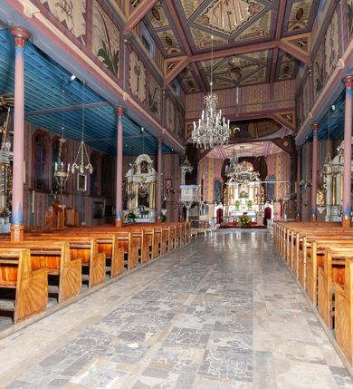 Zdjęcie nr 14: Kościół drewniany, o konstrukcji ramowej, na kamiennej podmurówce, elewacje jednolite, szalowane z listwowaniem o układzie pionowym z gzymsami pseudoarkadkowymi. Wieża zachodnia o konstrukcji słupowej, z szalunkiem o układzie poziomym z fryzem arkadkowym w górnej partii. Więźba dachowa drewniana, krokwiowa. Budynek na betonowym podmurowaniu przesłoniętym daszkiem gontowym. Kościół orientowany, trójnawowy, na rzucie wydłużonego krzyża, z płytkim transeptem, prezbiterium zakończone trójbocznie, z zakrystią przylegającą od południa, na skrzyżowaniu naw kopuła. Od zachodu wieża czterokondygnacyjna, na planie kwadratu przechodzącego w kwadrat o coraz bardziej ściętych narożach, ujęta dwiema kruchtami na rzucie kwadratu. Wnętrze o układzie bazylikowym, nawy podzielone smukłymi, żeliwnymi kolumienkami. Pomiędzy nawą a prezbiterium otwór tęczowy w formie kwadratu o ściętych narożach. Parapet chóru muzycznego w zachodniej części kościoła podparty na czterech kolumienkach. Nawa główna nakryta stropem z widocznymi elementami konstrukcji więźby, nawy boczne przekryte pułapami deskowymi. Posadzka z płyt kamiennych. Elewacja frontowa w formie wieży z dwoma kruchtami. Na każdej z trzech osi wejście z dwuskrzydłowymi drzwiami klepkowymi o układzie rombowym, z oknami w partii szczytu, nakryte daszkami okapowymi. Nad wejściem głównym żeliwna tabliczka z napisem „E(RZ)H(ERZOG) / ALBRECHT / 1888”. Na każdej kondygnacji wieży okna w formie stojącego prostokąta zwieńczone daszkami pulpitowymi, na pierwszej jedno, na drugiej trzy, na trzeciej cztery, na czwartej osiem. W elewacji północnej i południowej cztery podwójne otwory okienne w formie stojącego prostokąta o ściętych górnych narożach w partii naw bocznych oraz pięć okienek w formie leżącego prostokąta w partii nawy głównej. W elewacji południowej wejście z dwuskrzydłowymi drzwiami klepkowymi o układzie rombowym. Na osi skrzydeł transeptu po jednym otworze okiennym w formie stojącego prostokąta o ściętych górnych narożach. Na ścianie wschodniej prezbiterium Ogrójec w formie grupy Ukrzyżowania nakrytej daszkiem pulpitowym, flankowany dwoma otworami okiennymi w kształcie stojącego prostokąta o ściętych górnych narożach. Nawa główna nakryta dachem dwuspadowym. W połowie długości dachu oraz na skrzyżowaniu naw wznoszą się ponad kalenicą wieżyczki na sygnaturkę, na ośmiobocznym obitym blachą trzonie, z latarniami zwieńczonymi cebulastymi hełmami. Nad nawami bocznymi dachy pulpitowe, ramiona transeptu nakrywają dachy naczółkowe. Wieża zwieńczona dachem wieżowym, ośmiobocznym, z iglicą zakończoną krzyżem. 


