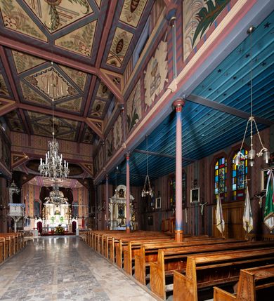 Zdjęcie nr 16: Kościół drewniany, o konstrukcji ramowej, na kamiennej podmurówce, elewacje jednolite, szalowane z listwowaniem o układzie pionowym z gzymsami pseudoarkadkowymi. Wieża zachodnia o konstrukcji słupowej, z szalunkiem o układzie poziomym z fryzem arkadkowym w górnej partii. Więźba dachowa drewniana, krokwiowa. Budynek na betonowym podmurowaniu przesłoniętym daszkiem gontowym. Kościół orientowany, trójnawowy, na rzucie wydłużonego krzyża, z płytkim transeptem, prezbiterium zakończone trójbocznie, z zakrystią przylegającą od południa, na skrzyżowaniu naw kopuła. Od zachodu wieża czterokondygnacyjna, na planie kwadratu przechodzącego w kwadrat o coraz bardziej ściętych narożach, ujęta dwiema kruchtami na rzucie kwadratu. Wnętrze o układzie bazylikowym, nawy podzielone smukłymi, żeliwnymi kolumienkami. Pomiędzy nawą a prezbiterium otwór tęczowy w formie kwadratu o ściętych narożach. Parapet chóru muzycznego w zachodniej części kościoła podparty na czterech kolumienkach. Nawa główna nakryta stropem z widocznymi elementami konstrukcji więźby, nawy boczne przekryte pułapami deskowymi. Posadzka z płyt kamiennych. Elewacja frontowa w formie wieży z dwoma kruchtami. Na każdej z trzech osi wejście z dwuskrzydłowymi drzwiami klepkowymi o układzie rombowym, z oknami w partii szczytu, nakryte daszkami okapowymi. Nad wejściem głównym żeliwna tabliczka z napisem „E(RZ)H(ERZOG) / ALBRECHT / 1888”. Na każdej kondygnacji wieży okna w formie stojącego prostokąta zwieńczone daszkami pulpitowymi, na pierwszej jedno, na drugiej trzy, na trzeciej cztery, na czwartej osiem. W elewacji północnej i południowej cztery podwójne otwory okienne w formie stojącego prostokąta o ściętych górnych narożach w partii naw bocznych oraz pięć okienek w formie leżącego prostokąta w partii nawy głównej. W elewacji południowej wejście z dwuskrzydłowymi drzwiami klepkowymi o układzie rombowym. Na osi skrzydeł transeptu po jednym otworze okiennym w formie stojącego prostokąta o ściętych górnych narożach. Na ścianie wschodniej prezbiterium Ogrójec w formie grupy Ukrzyżowania nakrytej daszkiem pulpitowym, flankowany dwoma otworami okiennymi w kształcie stojącego prostokąta o ściętych górnych narożach. Nawa główna nakryta dachem dwuspadowym. W połowie długości dachu oraz na skrzyżowaniu naw wznoszą się ponad kalenicą wieżyczki na sygnaturkę, na ośmiobocznym obitym blachą trzonie, z latarniami zwieńczonymi cebulastymi hełmami. Nad nawami bocznymi dachy pulpitowe, ramiona transeptu nakrywają dachy naczółkowe. Wieża zwieńczona dachem wieżowym, ośmiobocznym, z iglicą zakończoną krzyżem. 


