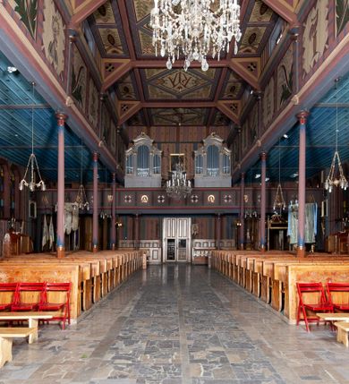 Zdjęcie nr 15: Kościół drewniany, o konstrukcji ramowej, na kamiennej podmurówce, elewacje jednolite, szalowane z listwowaniem o układzie pionowym z gzymsami pseudoarkadkowymi. Wieża zachodnia o konstrukcji słupowej, z szalunkiem o układzie poziomym z fryzem arkadkowym w górnej partii. Więźba dachowa drewniana, krokwiowa. Budynek na betonowym podmurowaniu przesłoniętym daszkiem gontowym. Kościół orientowany, trójnawowy, na rzucie wydłużonego krzyża, z płytkim transeptem, prezbiterium zakończone trójbocznie, z zakrystią przylegającą od południa, na skrzyżowaniu naw kopuła. Od zachodu wieża czterokondygnacyjna, na planie kwadratu przechodzącego w kwadrat o coraz bardziej ściętych narożach, ujęta dwiema kruchtami na rzucie kwadratu. Wnętrze o układzie bazylikowym, nawy podzielone smukłymi, żeliwnymi kolumienkami. Pomiędzy nawą a prezbiterium otwór tęczowy w formie kwadratu o ściętych narożach. Parapet chóru muzycznego w zachodniej części kościoła podparty na czterech kolumienkach. Nawa główna nakryta stropem z widocznymi elementami konstrukcji więźby, nawy boczne przekryte pułapami deskowymi. Posadzka z płyt kamiennych. Elewacja frontowa w formie wieży z dwoma kruchtami. Na każdej z trzech osi wejście z dwuskrzydłowymi drzwiami klepkowymi o układzie rombowym, z oknami w partii szczytu, nakryte daszkami okapowymi. Nad wejściem głównym żeliwna tabliczka z napisem „E(RZ)H(ERZOG) / ALBRECHT / 1888”. Na każdej kondygnacji wieży okna w formie stojącego prostokąta zwieńczone daszkami pulpitowymi, na pierwszej jedno, na drugiej trzy, na trzeciej cztery, na czwartej osiem. W elewacji północnej i południowej cztery podwójne otwory okienne w formie stojącego prostokąta o ściętych górnych narożach w partii naw bocznych oraz pięć okienek w formie leżącego prostokąta w partii nawy głównej. W elewacji południowej wejście z dwuskrzydłowymi drzwiami klepkowymi o układzie rombowym. Na osi skrzydeł transeptu po jednym otworze okiennym w formie stojącego prostokąta o ściętych górnych narożach. Na ścianie wschodniej prezbiterium Ogrójec w formie grupy Ukrzyżowania nakrytej daszkiem pulpitowym, flankowany dwoma otworami okiennymi w kształcie stojącego prostokąta o ściętych górnych narożach. Nawa główna nakryta dachem dwuspadowym. W połowie długości dachu oraz na skrzyżowaniu naw wznoszą się ponad kalenicą wieżyczki na sygnaturkę, na ośmiobocznym obitym blachą trzonie, z latarniami zwieńczonymi cebulastymi hełmami. Nad nawami bocznymi dachy pulpitowe, ramiona transeptu nakrywają dachy naczółkowe. Wieża zwieńczona dachem wieżowym, ośmiobocznym, z iglicą zakończoną krzyżem. 


