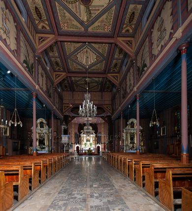 Zdjęcie nr 13: Kościół drewniany, o konstrukcji ramowej, na kamiennej podmurówce, elewacje jednolite, szalowane z listwowaniem o układzie pionowym z gzymsami pseudoarkadkowymi. Wieża zachodnia o konstrukcji słupowej, z szalunkiem o układzie poziomym z fryzem arkadkowym w górnej partii. Więźba dachowa drewniana, krokwiowa. Budynek na betonowym podmurowaniu przesłoniętym daszkiem gontowym. Kościół orientowany, trójnawowy, na rzucie wydłużonego krzyża, z płytkim transeptem, prezbiterium zakończone trójbocznie, z zakrystią przylegającą od południa, na skrzyżowaniu naw kopuła. Od zachodu wieża czterokondygnacyjna, na planie kwadratu przechodzącego w kwadrat o coraz bardziej ściętych narożach, ujęta dwiema kruchtami na rzucie kwadratu. Wnętrze o układzie bazylikowym, nawy podzielone smukłymi, żeliwnymi kolumienkami. Pomiędzy nawą a prezbiterium otwór tęczowy w formie kwadratu o ściętych narożach. Parapet chóru muzycznego w zachodniej części kościoła podparty na czterech kolumienkach. Nawa główna nakryta stropem z widocznymi elementami konstrukcji więźby, nawy boczne przekryte pułapami deskowymi. Posadzka z płyt kamiennych. Elewacja frontowa w formie wieży z dwoma kruchtami. Na każdej z trzech osi wejście z dwuskrzydłowymi drzwiami klepkowymi o układzie rombowym, z oknami w partii szczytu, nakryte daszkami okapowymi. Nad wejściem głównym żeliwna tabliczka z napisem „E(RZ)H(ERZOG) / ALBRECHT / 1888”. Na każdej kondygnacji wieży okna w formie stojącego prostokąta zwieńczone daszkami pulpitowymi, na pierwszej jedno, na drugiej trzy, na trzeciej cztery, na czwartej osiem. W elewacji północnej i południowej cztery podwójne otwory okienne w formie stojącego prostokąta o ściętych górnych narożach w partii naw bocznych oraz pięć okienek w formie leżącego prostokąta w partii nawy głównej. W elewacji południowej wejście z dwuskrzydłowymi drzwiami klepkowymi o układzie rombowym. Na osi skrzydeł transeptu po jednym otworze okiennym w formie stojącego prostokąta o ściętych górnych narożach. Na ścianie wschodniej prezbiterium Ogrójec w formie grupy Ukrzyżowania nakrytej daszkiem pulpitowym, flankowany dwoma otworami okiennymi w kształcie stojącego prostokąta o ściętych górnych narożach. Nawa główna nakryta dachem dwuspadowym. W połowie długości dachu oraz na skrzyżowaniu naw wznoszą się ponad kalenicą wieżyczki na sygnaturkę, na ośmiobocznym obitym blachą trzonie, z latarniami zwieńczonymi cebulastymi hełmami. Nad nawami bocznymi dachy pulpitowe, ramiona transeptu nakrywają dachy naczółkowe. Wieża zwieńczona dachem wieżowym, ośmiobocznym, z iglicą zakończoną krzyżem. 


