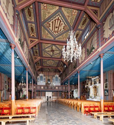 Zdjęcie nr 18: Kościół drewniany, o konstrukcji ramowej, na kamiennej podmurówce, elewacje jednolite, szalowane z listwowaniem o układzie pionowym z gzymsami pseudoarkadkowymi. Wieża zachodnia o konstrukcji słupowej, z szalunkiem o układzie poziomym z fryzem arkadkowym w górnej partii. Więźba dachowa drewniana, krokwiowa. Budynek na betonowym podmurowaniu przesłoniętym daszkiem gontowym. Kościół orientowany, trójnawowy, na rzucie wydłużonego krzyża, z płytkim transeptem, prezbiterium zakończone trójbocznie, z zakrystią przylegającą od południa, na skrzyżowaniu naw kopuła. Od zachodu wieża czterokondygnacyjna, na planie kwadratu przechodzącego w kwadrat o coraz bardziej ściętych narożach, ujęta dwiema kruchtami na rzucie kwadratu. Wnętrze o układzie bazylikowym, nawy podzielone smukłymi, żeliwnymi kolumienkami. Pomiędzy nawą a prezbiterium otwór tęczowy w formie kwadratu o ściętych narożach. Parapet chóru muzycznego w zachodniej części kościoła podparty na czterech kolumienkach. Nawa główna nakryta stropem z widocznymi elementami konstrukcji więźby, nawy boczne przekryte pułapami deskowymi. Posadzka z płyt kamiennych. Elewacja frontowa w formie wieży z dwoma kruchtami. Na każdej z trzech osi wejście z dwuskrzydłowymi drzwiami klepkowymi o układzie rombowym, z oknami w partii szczytu, nakryte daszkami okapowymi. Nad wejściem głównym żeliwna tabliczka z napisem „E(RZ)H(ERZOG) / ALBRECHT / 1888”. Na każdej kondygnacji wieży okna w formie stojącego prostokąta zwieńczone daszkami pulpitowymi, na pierwszej jedno, na drugiej trzy, na trzeciej cztery, na czwartej osiem. W elewacji północnej i południowej cztery podwójne otwory okienne w formie stojącego prostokąta o ściętych górnych narożach w partii naw bocznych oraz pięć okienek w formie leżącego prostokąta w partii nawy głównej. W elewacji południowej wejście z dwuskrzydłowymi drzwiami klepkowymi o układzie rombowym. Na osi skrzydeł transeptu po jednym otworze okiennym w formie stojącego prostokąta o ściętych górnych narożach. Na ścianie wschodniej prezbiterium Ogrójec w formie grupy Ukrzyżowania nakrytej daszkiem pulpitowym, flankowany dwoma otworami okiennymi w kształcie stojącego prostokąta o ściętych górnych narożach. Nawa główna nakryta dachem dwuspadowym. W połowie długości dachu oraz na skrzyżowaniu naw wznoszą się ponad kalenicą wieżyczki na sygnaturkę, na ośmiobocznym obitym blachą trzonie, z latarniami zwieńczonymi cebulastymi hełmami. Nad nawami bocznymi dachy pulpitowe, ramiona transeptu nakrywają dachy naczółkowe. Wieża zwieńczona dachem wieżowym, ośmiobocznym, z iglicą zakończoną krzyżem. 


