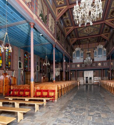 Zdjęcie nr 17: Kościół drewniany, o konstrukcji ramowej, na kamiennej podmurówce, elewacje jednolite, szalowane z listwowaniem o układzie pionowym z gzymsami pseudoarkadkowymi. Wieża zachodnia o konstrukcji słupowej, z szalunkiem o układzie poziomym z fryzem arkadkowym w górnej partii. Więźba dachowa drewniana, krokwiowa. Budynek na betonowym podmurowaniu przesłoniętym daszkiem gontowym. Kościół orientowany, trójnawowy, na rzucie wydłużonego krzyża, z płytkim transeptem, prezbiterium zakończone trójbocznie, z zakrystią przylegającą od południa, na skrzyżowaniu naw kopuła. Od zachodu wieża czterokondygnacyjna, na planie kwadratu przechodzącego w kwadrat o coraz bardziej ściętych narożach, ujęta dwiema kruchtami na rzucie kwadratu. Wnętrze o układzie bazylikowym, nawy podzielone smukłymi, żeliwnymi kolumienkami. Pomiędzy nawą a prezbiterium otwór tęczowy w formie kwadratu o ściętych narożach. Parapet chóru muzycznego w zachodniej części kościoła podparty na czterech kolumienkach. Nawa główna nakryta stropem z widocznymi elementami konstrukcji więźby, nawy boczne przekryte pułapami deskowymi. Posadzka z płyt kamiennych. Elewacja frontowa w formie wieży z dwoma kruchtami. Na każdej z trzech osi wejście z dwuskrzydłowymi drzwiami klepkowymi o układzie rombowym, z oknami w partii szczytu, nakryte daszkami okapowymi. Nad wejściem głównym żeliwna tabliczka z napisem „E(RZ)H(ERZOG) / ALBRECHT / 1888”. Na każdej kondygnacji wieży okna w formie stojącego prostokąta zwieńczone daszkami pulpitowymi, na pierwszej jedno, na drugiej trzy, na trzeciej cztery, na czwartej osiem. W elewacji północnej i południowej cztery podwójne otwory okienne w formie stojącego prostokąta o ściętych górnych narożach w partii naw bocznych oraz pięć okienek w formie leżącego prostokąta w partii nawy głównej. W elewacji południowej wejście z dwuskrzydłowymi drzwiami klepkowymi o układzie rombowym. Na osi skrzydeł transeptu po jednym otworze okiennym w formie stojącego prostokąta o ściętych górnych narożach. Na ścianie wschodniej prezbiterium Ogrójec w formie grupy Ukrzyżowania nakrytej daszkiem pulpitowym, flankowany dwoma otworami okiennymi w kształcie stojącego prostokąta o ściętych górnych narożach. Nawa główna nakryta dachem dwuspadowym. W połowie długości dachu oraz na skrzyżowaniu naw wznoszą się ponad kalenicą wieżyczki na sygnaturkę, na ośmiobocznym obitym blachą trzonie, z latarniami zwieńczonymi cebulastymi hełmami. Nad nawami bocznymi dachy pulpitowe, ramiona transeptu nakrywają dachy naczółkowe. Wieża zwieńczona dachem wieżowym, ośmiobocznym, z iglicą zakończoną krzyżem. 


