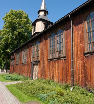 Zdjęcie nr 6: Kościół drewniany, o konstrukcji ramowej, na kamiennej podmurówce, elewacje jednolite, szalowane z listwowaniem o układzie pionowym z gzymsami pseudoarkadkowymi. Wieża zachodnia o konstrukcji słupowej, z szalunkiem o układzie poziomym z fryzem arkadkowym w górnej partii. Więźba dachowa drewniana, krokwiowa. Budynek na betonowym podmurowaniu przesłoniętym daszkiem gontowym. Kościół orientowany, trójnawowy, na rzucie wydłużonego krzyża, z płytkim transeptem, prezbiterium zakończone trójbocznie, z zakrystią przylegającą od południa, na skrzyżowaniu naw kopuła. Od zachodu wieża czterokondygnacyjna, na planie kwadratu przechodzącego w kwadrat o coraz bardziej ściętych narożach, ujęta dwiema kruchtami na rzucie kwadratu. Wnętrze o układzie bazylikowym, nawy podzielone smukłymi, żeliwnymi kolumienkami. Pomiędzy nawą a prezbiterium otwór tęczowy w formie kwadratu o ściętych narożach. Parapet chóru muzycznego w zachodniej części kościoła podparty na czterech kolumienkach. Nawa główna nakryta stropem z widocznymi elementami konstrukcji więźby, nawy boczne przekryte pułapami deskowymi. Posadzka z płyt kamiennych. Elewacja frontowa w formie wieży z dwoma kruchtami. Na każdej z trzech osi wejście z dwuskrzydłowymi drzwiami klepkowymi o układzie rombowym, z oknami w partii szczytu, nakryte daszkami okapowymi. Nad wejściem głównym żeliwna tabliczka z napisem „E(RZ)H(ERZOG) / ALBRECHT / 1888”. Na każdej kondygnacji wieży okna w formie stojącego prostokąta zwieńczone daszkami pulpitowymi, na pierwszej jedno, na drugiej trzy, na trzeciej cztery, na czwartej osiem. W elewacji północnej i południowej cztery podwójne otwory okienne w formie stojącego prostokąta o ściętych górnych narożach w partii naw bocznych oraz pięć okienek w formie leżącego prostokąta w partii nawy głównej. W elewacji południowej wejście z dwuskrzydłowymi drzwiami klepkowymi o układzie rombowym. Na osi skrzydeł transeptu po jednym otworze okiennym w formie stojącego prostokąta o ściętych górnych narożach. Na ścianie wschodniej prezbiterium Ogrójec w formie grupy Ukrzyżowania nakrytej daszkiem pulpitowym, flankowany dwoma otworami okiennymi w kształcie stojącego prostokąta o ściętych górnych narożach. Nawa główna nakryta dachem dwuspadowym. W połowie długości dachu oraz na skrzyżowaniu naw wznoszą się ponad kalenicą wieżyczki na sygnaturkę, na ośmiobocznym obitym blachą trzonie, z latarniami zwieńczonymi cebulastymi hełmami. Nad nawami bocznymi dachy pulpitowe, ramiona transeptu nakrywają dachy naczółkowe. Wieża zwieńczona dachem wieżowym, ośmiobocznym, z iglicą zakończoną krzyżem. 


