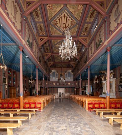 Zdjęcie nr 22: Kościół drewniany, o konstrukcji ramowej, na kamiennej podmurówce, elewacje jednolite, szalowane z listwowaniem o układzie pionowym z gzymsami pseudoarkadkowymi. Wieża zachodnia o konstrukcji słupowej, z szalunkiem o układzie poziomym z fryzem arkadkowym w górnej partii. Więźba dachowa drewniana, krokwiowa. Budynek na betonowym podmurowaniu przesłoniętym daszkiem gontowym. Kościół orientowany, trójnawowy, na rzucie wydłużonego krzyża, z płytkim transeptem, prezbiterium zakończone trójbocznie, z zakrystią przylegającą od południa, na skrzyżowaniu naw kopuła. Od zachodu wieża czterokondygnacyjna, na planie kwadratu przechodzącego w kwadrat o coraz bardziej ściętych narożach, ujęta dwiema kruchtami na rzucie kwadratu. Wnętrze o układzie bazylikowym, nawy podzielone smukłymi, żeliwnymi kolumienkami. Pomiędzy nawą a prezbiterium otwór tęczowy w formie kwadratu o ściętych narożach. Parapet chóru muzycznego w zachodniej części kościoła podparty na czterech kolumienkach. Nawa główna nakryta stropem z widocznymi elementami konstrukcji więźby, nawy boczne przekryte pułapami deskowymi. Posadzka z płyt kamiennych. Elewacja frontowa w formie wieży z dwoma kruchtami. Na każdej z trzech osi wejście z dwuskrzydłowymi drzwiami klepkowymi o układzie rombowym, z oknami w partii szczytu, nakryte daszkami okapowymi. Nad wejściem głównym żeliwna tabliczka z napisem „E(RZ)H(ERZOG) / ALBRECHT / 1888”. Na każdej kondygnacji wieży okna w formie stojącego prostokąta zwieńczone daszkami pulpitowymi, na pierwszej jedno, na drugiej trzy, na trzeciej cztery, na czwartej osiem. W elewacji północnej i południowej cztery podwójne otwory okienne w formie stojącego prostokąta o ściętych górnych narożach w partii naw bocznych oraz pięć okienek w formie leżącego prostokąta w partii nawy głównej. W elewacji południowej wejście z dwuskrzydłowymi drzwiami klepkowymi o układzie rombowym. Na osi skrzydeł transeptu po jednym otworze okiennym w formie stojącego prostokąta o ściętych górnych narożach. Na ścianie wschodniej prezbiterium Ogrójec w formie grupy Ukrzyżowania nakrytej daszkiem pulpitowym, flankowany dwoma otworami okiennymi w kształcie stojącego prostokąta o ściętych górnych narożach. Nawa główna nakryta dachem dwuspadowym. W połowie długości dachu oraz na skrzyżowaniu naw wznoszą się ponad kalenicą wieżyczki na sygnaturkę, na ośmiobocznym obitym blachą trzonie, z latarniami zwieńczonymi cebulastymi hełmami. Nad nawami bocznymi dachy pulpitowe, ramiona transeptu nakrywają dachy naczółkowe. Wieża zwieńczona dachem wieżowym, ośmiobocznym, z iglicą zakończoną krzyżem. 


