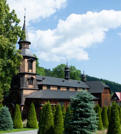 Zdjęcie nr 1: Kościół drewniany, o konstrukcji ramowej, na kamiennej podmurówce, elewacje jednolite, szalowane z listwowaniem o układzie pionowym z gzymsami pseudoarkadkowymi. Wieża zachodnia o konstrukcji słupowej, z szalunkiem o układzie poziomym z fryzem arkadkowym w górnej partii. Więźba dachowa drewniana, krokwiowa. Budynek na betonowym podmurowaniu przesłoniętym daszkiem gontowym. Kościół orientowany, trójnawowy, na rzucie wydłużonego krzyża, z płytkim transeptem, prezbiterium zakończone trójbocznie, z zakrystią przylegającą od południa, na skrzyżowaniu naw kopuła. Od zachodu wieża czterokondygnacyjna, na planie kwadratu przechodzącego w kwadrat o coraz bardziej ściętych narożach, ujęta dwiema kruchtami na rzucie kwadratu. Wnętrze o układzie bazylikowym, nawy podzielone smukłymi, żeliwnymi kolumienkami. Pomiędzy nawą a prezbiterium otwór tęczowy w formie kwadratu o ściętych narożach. Parapet chóru muzycznego w zachodniej części kościoła podparty na czterech kolumienkach. Nawa główna nakryta stropem z widocznymi elementami konstrukcji więźby, nawy boczne przekryte pułapami deskowymi. Posadzka z płyt kamiennych. Elewacja frontowa w formie wieży z dwoma kruchtami. Na każdej z trzech osi wejście z dwuskrzydłowymi drzwiami klepkowymi o układzie rombowym, z oknami w partii szczytu, nakryte daszkami okapowymi. Nad wejściem głównym żeliwna tabliczka z napisem „E(RZ)H(ERZOG) / ALBRECHT / 1888”. Na każdej kondygnacji wieży okna w formie stojącego prostokąta zwieńczone daszkami pulpitowymi, na pierwszej jedno, na drugiej trzy, na trzeciej cztery, na czwartej osiem. W elewacji północnej i południowej cztery podwójne otwory okienne w formie stojącego prostokąta o ściętych górnych narożach w partii naw bocznych oraz pięć okienek w formie leżącego prostokąta w partii nawy głównej. W elewacji południowej wejście z dwuskrzydłowymi drzwiami klepkowymi o układzie rombowym. Na osi skrzydeł transeptu po jednym otworze okiennym w formie stojącego prostokąta o ściętych górnych narożach. Na ścianie wschodniej prezbiterium Ogrójec w formie grupy Ukrzyżowania nakrytej daszkiem pulpitowym, flankowany dwoma otworami okiennymi w kształcie stojącego prostokąta o ściętych górnych narożach. Nawa główna nakryta dachem dwuspadowym. W połowie długości dachu oraz na skrzyżowaniu naw wznoszą się ponad kalenicą wieżyczki na sygnaturkę, na ośmiobocznym obitym blachą trzonie, z latarniami zwieńczonymi cebulastymi hełmami. Nad nawami bocznymi dachy pulpitowe, ramiona transeptu nakrywają dachy naczółkowe. Wieża zwieńczona dachem wieżowym, ośmiobocznym, z iglicą zakończoną krzyżem. 


