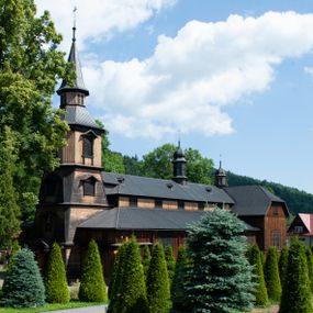 Zdjęcie nr 1: Kościół drewniany, o konstrukcji ramowej, na kamiennej podmurówce, elewacje jednolite, szalowane z listwowaniem o układzie pionowym z gzymsami pseudoarkadkowymi. Wieża zachodnia o konstrukcji słupowej, z szalunkiem o układzie poziomym z fryzem arkadkowym w górnej partii. Więźba dachowa drewniana, krokwiowa. Budynek na betonowym podmurowaniu przesłoniętym daszkiem gontowym. Kościół orientowany, trójnawowy, na rzucie wydłużonego krzyża, z płytkim transeptem, prezbiterium zakończone trójbocznie, z zakrystią przylegającą od południa, na skrzyżowaniu naw kopuła. Od zachodu wieża czterokondygnacyjna, na planie kwadratu przechodzącego w kwadrat o coraz bardziej ściętych narożach, ujęta dwiema kruchtami na rzucie kwadratu. Wnętrze o układzie bazylikowym, nawy podzielone smukłymi, żeliwnymi kolumienkami. Pomiędzy nawą a prezbiterium otwór tęczowy w formie kwadratu o ściętych narożach. Parapet chóru muzycznego w zachodniej części kościoła podparty na czterech kolumienkach. Nawa główna nakryta stropem z widocznymi elementami konstrukcji więźby, nawy boczne przekryte pułapami deskowymi. Posadzka z płyt kamiennych. Elewacja frontowa w formie wieży z dwoma kruchtami. Na każdej z trzech osi wejście z dwuskrzydłowymi drzwiami klepkowymi o układzie rombowym, z oknami w partii szczytu, nakryte daszkami okapowymi. Nad wejściem głównym żeliwna tabliczka z napisem „E(RZ)H(ERZOG) / ALBRECHT / 1888”. Na każdej kondygnacji wieży okna w formie stojącego prostokąta zwieńczone daszkami pulpitowymi, na pierwszej jedno, na drugiej trzy, na trzeciej cztery, na czwartej osiem. W elewacji północnej i południowej cztery podwójne otwory okienne w formie stojącego prostokąta o ściętych górnych narożach w partii naw bocznych oraz pięć okienek w formie leżącego prostokąta w partii nawy głównej. W elewacji południowej wejście z dwuskrzydłowymi drzwiami klepkowymi o układzie rombowym. Na osi skrzydeł transeptu po jednym otworze okiennym w formie stojącego prostokąta o ściętych górnych narożach. Na ścianie wschodniej prezbiterium Ogrójec w formie grupy Ukrzyżowania nakrytej daszkiem pulpitowym, flankowany dwoma otworami okiennymi w kształcie stojącego prostokąta o ściętych górnych narożach. Nawa główna nakryta dachem dwuspadowym. W połowie długości dachu oraz na skrzyżowaniu naw wznoszą się ponad kalenicą wieżyczki na sygnaturkę, na ośmiobocznym obitym blachą trzonie, z latarniami zwieńczonymi cebulastymi hełmami. Nad nawami bocznymi dachy pulpitowe, ramiona transeptu nakrywają dachy naczółkowe. Wieża zwieńczona dachem wieżowym, ośmiobocznym, z iglicą zakończoną krzyżem. 


