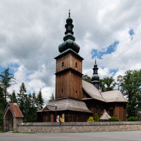 Zdjęcie nr 1: Kościół drewniany o konstrukcji zrębowej, elewacje jednolite, szalowane z listwowaniem, wzmocnione lisicami, wieża o konstrukcji słupowej. Więźba dachowa drewniana, krokwiowa. Budynek na kamiennym podmurowaniu przesłoniętym daszkiem gontowym. Kościół orientowany, jednonawowy z dwiema kaplicami o charakterze transeptu zamkniętymi wielobocznie, na planie krzyża łacińskiego, o węższym prezbiterium zamkniętym trójbocznie. Do wschodniej ściany prezbiterium przylega ogrójec w formie kapliczki, od północy zakrystia na planie prostokąta. Na skrzyżowaniu nawy z południowym ramieniem transeptu kruchta na planie prostokąta. Od zachodu do nawy przylega wieża na planie kwadratu, otoczona sobotami. Prezbiterium i nawa nakryte pozornym sklepieniem tej samej szerokości, obwiedzionym dużym, profilowanym gzymsem podtrzymywanym w nawie przez dwie pary filarów o kanelowanych trzonach, na cokołach. Sklepieniu nawy głównej towarzyszą płaskie i niższe stropy z fasetami w przestrzeniach bocznych. Ściany boczne nawy zwieńczone profilowanym gzymsem. Pomiędzy nawą a prezbiterium otwór tęczowy w formie odcinkowej arkady podtrzymywanej przez filary o kanelowanych trzonach z belką o falistym zarysie. Kaplice boczne otwarte do nawy odcinkowymi arkadami podtrzymywanymi przez filary o kanelowanych trzonach, na cokołach. Parapet chóru muzycznego w zachodniej części nawy, o wybrzuszonej środkowej części, podparty na dwóch filarach o kanelowanych trzonach, na cokołach. Posadzka z płyt ceramicznych. Elewacja frontowa w postaci wieży otoczonej sobotami. Na osi frontowej ściany sobót płytka kruchta zwieńczona gzymsem z przyczółkiem wypełnionym motywem „słoneczka”, przykryta dwuspadowym dachem. Drzwi dwuskrzydłowe, drewniane z okuciami. Korpus wieży podzielony poziomo daszkiem okapowym w dwóch trzecich wysokości, na froncie okno. W dolnej części małe otwory dzwonne z trzech stron, w górnej części duże otwory dzwonne z czterech stron. Wieża zwieńczona hełmem baniastym z latarnią. Ściany sobót szalowane z poziomym listwowaniem, przekryte mansardowym dachem gontowym, na północnej i południowej ścianie dwie pary okien w formie leżącego prostokąta zamkniętego łukiem odcinkowym. W elewacji południowej cztery otwory okienne w formie stojącego prostokąta zamkniętego łukiem odcinkowym, w partii prezbiterium z witrażami. Na elewacji wschodniej ogrójec w formie nadwieszonej kapliczki nakrytej dwuspadowym daszkiem z grupą Ukrzyżowania. W elewacji północnej dwa otwory okienne w formie stojącego prostokąta zamkniętego łukiem odcinkowym. W zakrystii małe kwadratowe okienko. W obu ramionach transeptu analogiczne jak w elewacjach otwory okienne na wschodniej i zachodniej ścianie. Kościół nakryty dachami gontowymi, wyższym nad nawą, niższym nad prezbiterium, dwuspadowym nad nawą oraz wielospadowym nad prezbiterium i ramionami transeptu; nad zakrystią i kruchtą boczną dachy dwuspadowe. W połowie długości dachu, nad nawą, od strony prezbiterium wznosi się ponad kalenicą wieżyczka na sygnaturkę, obita blachą, na ośmiobocznym trzonie, z latarnią zwieńczoną niewielkim baniastym hełmem z latarnią.
