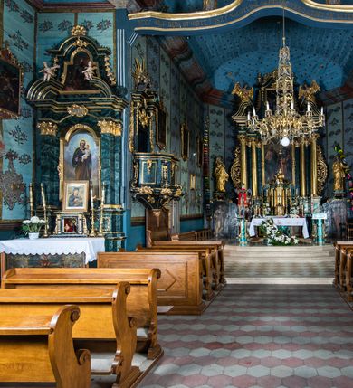 Zdjęcie nr 70: Kościół drewniany o konstrukcji zrębowej, elewacje jednolite, szalowane z listwowaniem, wzmocnione lisicami, wieża o konstrukcji słupowej. Więźba dachowa drewniana, krokwiowa. Budynek na kamiennym podmurowaniu przesłoniętym daszkiem gontowym. Kościół orientowany, jednonawowy z dwiema kaplicami o charakterze transeptu zamkniętymi wielobocznie, na planie krzyża łacińskiego, o węższym prezbiterium zamkniętym trójbocznie. Do wschodniej ściany prezbiterium przylega ogrójec w formie kapliczki, od północy zakrystia na planie prostokąta. Na skrzyżowaniu nawy z południowym ramieniem transeptu kruchta na planie prostokąta. Od zachodu do nawy przylega wieża na planie kwadratu, otoczona sobotami. Prezbiterium i nawa nakryte pozornym sklepieniem tej samej szerokości, obwiedzionym dużym, profilowanym gzymsem podtrzymywanym w nawie przez dwie pary filarów o kanelowanych trzonach, na cokołach. Sklepieniu nawy głównej towarzyszą płaskie i niższe stropy z fasetami w przestrzeniach bocznych. Ściany boczne nawy zwieńczone profilowanym gzymsem. Pomiędzy nawą a prezbiterium otwór tęczowy w formie odcinkowej arkady podtrzymywanej przez filary o kanelowanych trzonach z belką o falistym zarysie. Kaplice boczne otwarte do nawy odcinkowymi arkadami podtrzymywanymi przez filary o kanelowanych trzonach, na cokołach. Parapet chóru muzycznego w zachodniej części nawy, o wybrzuszonej środkowej części, podparty na dwóch filarach o kanelowanych trzonach, na cokołach. Posadzka z płyt ceramicznych. Elewacja frontowa w postaci wieży otoczonej sobotami. Na osi frontowej ściany sobót płytka kruchta zwieńczona gzymsem z przyczółkiem wypełnionym motywem „słoneczka”, przykryta dwuspadowym dachem. Drzwi dwuskrzydłowe, drewniane z okuciami. Korpus wieży podzielony poziomo daszkiem okapowym w dwóch trzecich wysokości, na froncie okno. W dolnej części małe otwory dzwonne z trzech stron, w górnej części duże otwory dzwonne z czterech stron. Wieża zwieńczona hełmem baniastym z latarnią. Ściany sobót szalowane z poziomym listwowaniem, przekryte mansardowym dachem gontowym, na północnej i południowej ścianie dwie pary okien w formie leżącego prostokąta zamkniętego łukiem odcinkowym. W elewacji południowej cztery otwory okienne w formie stojącego prostokąta zamkniętego łukiem odcinkowym, w partii prezbiterium z witrażami. Na elewacji wschodniej ogrójec w formie nadwieszonej kapliczki nakrytej dwuspadowym daszkiem z grupą Ukrzyżowania. W elewacji północnej dwa otwory okienne w formie stojącego prostokąta zamkniętego łukiem odcinkowym. W zakrystii małe kwadratowe okienko. W obu ramionach transeptu analogiczne jak w elewacjach otwory okienne na wschodniej i zachodniej ścianie. Kościół nakryty dachami gontowymi, wyższym nad nawą, niższym nad prezbiterium, dwuspadowym nad nawą oraz wielospadowym nad prezbiterium i ramionami transeptu; nad zakrystią i kruchtą boczną dachy dwuspadowe. W połowie długości dachu, nad nawą, od strony prezbiterium wznosi się ponad kalenicą wieżyczka na sygnaturkę, obita blachą, na ośmiobocznym trzonie, z latarnią zwieńczoną niewielkim baniastym hełmem z latarnią.
