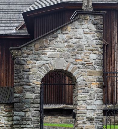 Zdjęcie nr 59: Kościół drewniany o konstrukcji zrębowej, elewacje jednolite, szalowane z listwowaniem, wzmocnione lisicami, wieża o konstrukcji słupowej. Więźba dachowa drewniana, krokwiowa. Budynek na kamiennym podmurowaniu przesłoniętym daszkiem gontowym. Kościół orientowany, jednonawowy z dwiema kaplicami o charakterze transeptu zamkniętymi wielobocznie, na planie krzyża łacińskiego, o węższym prezbiterium zamkniętym trójbocznie. Do wschodniej ściany prezbiterium przylega ogrójec w formie kapliczki, od północy zakrystia na planie prostokąta. Na skrzyżowaniu nawy z południowym ramieniem transeptu kruchta na planie prostokąta. Od zachodu do nawy przylega wieża na planie kwadratu, otoczona sobotami. Prezbiterium i nawa nakryte pozornym sklepieniem tej samej szerokości, obwiedzionym dużym, profilowanym gzymsem podtrzymywanym w nawie przez dwie pary filarów o kanelowanych trzonach, na cokołach. Sklepieniu nawy głównej towarzyszą płaskie i niższe stropy z fasetami w przestrzeniach bocznych. Ściany boczne nawy zwieńczone profilowanym gzymsem. Pomiędzy nawą a prezbiterium otwór tęczowy w formie odcinkowej arkady podtrzymywanej przez filary o kanelowanych trzonach z belką o falistym zarysie. Kaplice boczne otwarte do nawy odcinkowymi arkadami podtrzymywanymi przez filary o kanelowanych trzonach, na cokołach. Parapet chóru muzycznego w zachodniej części nawy, o wybrzuszonej środkowej części, podparty na dwóch filarach o kanelowanych trzonach, na cokołach. Posadzka z płyt ceramicznych. Elewacja frontowa w postaci wieży otoczonej sobotami. Na osi frontowej ściany sobót płytka kruchta zwieńczona gzymsem z przyczółkiem wypełnionym motywem „słoneczka”, przykryta dwuspadowym dachem. Drzwi dwuskrzydłowe, drewniane z okuciami. Korpus wieży podzielony poziomo daszkiem okapowym w dwóch trzecich wysokości, na froncie okno. W dolnej części małe otwory dzwonne z trzech stron, w górnej części duże otwory dzwonne z czterech stron. Wieża zwieńczona hełmem baniastym z latarnią. Ściany sobót szalowane z poziomym listwowaniem, przekryte mansardowym dachem gontowym, na północnej i południowej ścianie dwie pary okien w formie leżącego prostokąta zamkniętego łukiem odcinkowym. W elewacji południowej cztery otwory okienne w formie stojącego prostokąta zamkniętego łukiem odcinkowym, w partii prezbiterium z witrażami. Na elewacji wschodniej ogrójec w formie nadwieszonej kapliczki nakrytej dwuspadowym daszkiem z grupą Ukrzyżowania. W elewacji północnej dwa otwory okienne w formie stojącego prostokąta zamkniętego łukiem odcinkowym. W zakrystii małe kwadratowe okienko. W obu ramionach transeptu analogiczne jak w elewacjach otwory okienne na wschodniej i zachodniej ścianie. Kościół nakryty dachami gontowymi, wyższym nad nawą, niższym nad prezbiterium, dwuspadowym nad nawą oraz wielospadowym nad prezbiterium i ramionami transeptu; nad zakrystią i kruchtą boczną dachy dwuspadowe. W połowie długości dachu, nad nawą, od strony prezbiterium wznosi się ponad kalenicą wieżyczka na sygnaturkę, obita blachą, na ośmiobocznym trzonie, z latarnią zwieńczoną niewielkim baniastym hełmem z latarnią.
