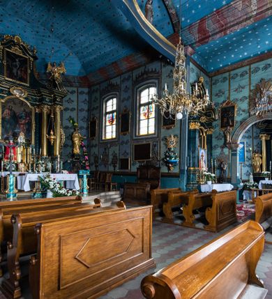 Zdjęcie nr 4: Kościół drewniany o konstrukcji zrębowej, elewacje jednolite, szalowane z listwowaniem, wzmocnione lisicami, wieża o konstrukcji słupowej. Więźba dachowa drewniana, krokwiowa. Budynek na kamiennym podmurowaniu przesłoniętym daszkiem gontowym. Kościół orientowany, jednonawowy z dwiema kaplicami o charakterze transeptu zamkniętymi wielobocznie, na planie krzyża łacińskiego, o węższym prezbiterium zamkniętym trójbocznie. Do wschodniej ściany prezbiterium przylega ogrójec w formie kapliczki, od północy zakrystia na planie prostokąta. Na skrzyżowaniu nawy z południowym ramieniem transeptu kruchta na planie prostokąta. Od zachodu do nawy przylega wieża na planie kwadratu, otoczona sobotami. Prezbiterium i nawa nakryte pozornym sklepieniem tej samej szerokości, obwiedzionym dużym, profilowanym gzymsem podtrzymywanym w nawie przez dwie pary filarów o kanelowanych trzonach, na cokołach. Sklepieniu nawy głównej towarzyszą płaskie i niższe stropy z fasetami w przestrzeniach bocznych. Ściany boczne nawy zwieńczone profilowanym gzymsem. Pomiędzy nawą a prezbiterium otwór tęczowy w formie odcinkowej arkady podtrzymywanej przez filary o kanelowanych trzonach z belką o falistym zarysie. Kaplice boczne otwarte do nawy odcinkowymi arkadami podtrzymywanymi przez filary o kanelowanych trzonach, na cokołach. Parapet chóru muzycznego w zachodniej części nawy, o wybrzuszonej środkowej części, podparty na dwóch filarach o kanelowanych trzonach, na cokołach. Posadzka z płyt ceramicznych. Elewacja frontowa w postaci wieży otoczonej sobotami. Na osi frontowej ściany sobót płytka kruchta zwieńczona gzymsem z przyczółkiem wypełnionym motywem „słoneczka”, przykryta dwuspadowym dachem. Drzwi dwuskrzydłowe, drewniane z okuciami. Korpus wieży podzielony poziomo daszkiem okapowym w dwóch trzecich wysokości, na froncie okno. W dolnej części małe otwory dzwonne z trzech stron, w górnej części duże otwory dzwonne z czterech stron. Wieża zwieńczona hełmem baniastym z latarnią. Ściany sobót szalowane z poziomym listwowaniem, przekryte mansardowym dachem gontowym, na północnej i południowej ścianie dwie pary okien w formie leżącego prostokąta zamkniętego łukiem odcinkowym. W elewacji południowej cztery otwory okienne w formie stojącego prostokąta zamkniętego łukiem odcinkowym, w partii prezbiterium z witrażami. Na elewacji wschodniej ogrójec w formie nadwieszonej kapliczki nakrytej dwuspadowym daszkiem z grupą Ukrzyżowania. W elewacji północnej dwa otwory okienne w formie stojącego prostokąta zamkniętego łukiem odcinkowym. W zakrystii małe kwadratowe okienko. W obu ramionach transeptu analogiczne jak w elewacjach otwory okienne na wschodniej i zachodniej ścianie. Kościół nakryty dachami gontowymi, wyższym nad nawą, niższym nad prezbiterium, dwuspadowym nad nawą oraz wielospadowym nad prezbiterium i ramionami transeptu; nad zakrystią i kruchtą boczną dachy dwuspadowe. W połowie długości dachu, nad nawą, od strony prezbiterium wznosi się ponad kalenicą wieżyczka na sygnaturkę, obita blachą, na ośmiobocznym trzonie, z latarnią zwieńczoną niewielkim baniastym hełmem z latarnią.

