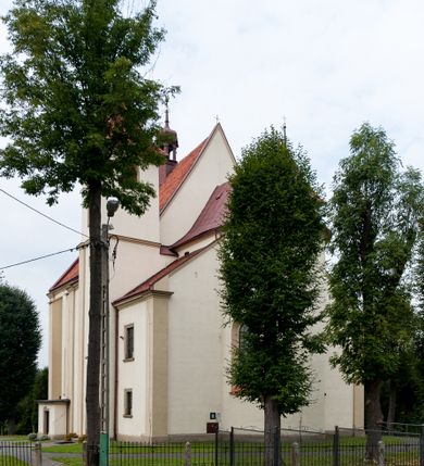 Zdjęcie nr 4: Kościół jest jednonawowy, trójprzęsłowy, z płytkimi kaplicami tworzącymi pseudotransept i jednoprzęsłowym prezbiterium zakończonym apsydą. Do prezbiterium przylegają dwa aneksy mieszące w przyziemiu zakrystię i skarbczyk, a na piętrze empory otwarte na prezbiterium. Do nawy od południa dostawiona jest kruchta. W naroża między kaplicami a nawą wstawiono dwie wieże-dzwonnice z klatkami schodowymi prowadzącymi na empory. Nawa jest rozczłonkowana płaskimi, szerokimi pilastrami toskańskimi, a nakryta sklepieniem kolebkowym z lunetami; prezbiterium przykryte sklepieniem kolebkowym z żebrami spływającymi na wsporniki, apsyda sklepieniem parasolowatym.  Prezbiterium ujęte dwiema głębokimi, półkoliście zamkniętymi wnękami, nad którymi parapety empor z ślepymi arkadkami z balasów jenolalkowych i łuków półkolistych. Wnętrze oświetlają wysokie i szerokie okna zamknięte półkoliście. W aneksach przy prezbiterium i w emporach znajdują się okna prostokątne. Fasada dwustrefowa, trójosiowa, ale osie i strefy wyznaczone jedynie przez okna, drzwi i nisze, zamknięta trójkątnie.    
Portal prostokątnych drzwi utworzony z pary żłobkowanych, toskańskich pilastrów, podtrzymujących belkowanie z trójkątnym przyczółkiem. Fryz belkowania ozdobiony tryglifami z łezkami i metopami w kształcie rozet i talerzy, a przyczółek kostkowaniem. Nad portalem okno w głębokim rozglifieniu, w kształcie prostokąta zamkniętego półkoliście. Po bokach portalu i okna głębokie nisze ujęte od dołu i góry odcinkami gzymsu. Zewnętrzne elewacje ujęte częściowo szkarpami, częściowo lizenami. W wieżach wejścia do kościoła i na klatki schodowe oraz niewielkie okienka w klatce schodowej i prześwity zamknięte półkoliście w dzwonnicach. Dachy dwuspadowe, na wieżach czterospadowe, nad nawą, wieżami i aneksami przy prezbiterium kryte dachówką, nad prezbiterium blachą. Na dachu wieżyczka na sygnaturkę. 
