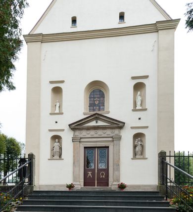 Zdjęcie nr 12: Kościół jest jednonawowy, trójprzęsłowy, z płytkimi kaplicami tworzącymi pseudotransept i jednoprzęsłowym prezbiterium zakończonym apsydą. Do prezbiterium przylegają dwa aneksy mieszące w przyziemiu zakrystię i skarbczyk, a na piętrze empory otwarte na prezbiterium. Do nawy od południa dostawiona jest kruchta. W naroża między kaplicami a nawą wstawiono dwie wieże-dzwonnice z klatkami schodowymi prowadzącymi na empory. Nawa jest rozczłonkowana płaskimi, szerokimi pilastrami toskańskimi, a nakryta sklepieniem kolebkowym z lunetami; prezbiterium przykryte sklepieniem kolebkowym z żebrami spływającymi na wsporniki, apsyda sklepieniem parasolowatym.  Prezbiterium ujęte dwiema głębokimi, półkoliście zamkniętymi wnękami, nad którymi parapety empor z ślepymi arkadkami z balasów jenolalkowych i łuków półkolistych. Wnętrze oświetlają wysokie i szerokie okna zamknięte półkoliście. W aneksach przy prezbiterium i w emporach znajdują się okna prostokątne. Fasada dwustrefowa, trójosiowa, ale osie i strefy wyznaczone jedynie przez okna, drzwi i nisze, zamknięta trójkątnie.    
Portal prostokątnych drzwi utworzony z pary żłobkowanych, toskańskich pilastrów, podtrzymujących belkowanie z trójkątnym przyczółkiem. Fryz belkowania ozdobiony tryglifami z łezkami i metopami w kształcie rozet i talerzy, a przyczółek kostkowaniem. Nad portalem okno w głębokim rozglifieniu, w kształcie prostokąta zamkniętego półkoliście. Po bokach portalu i okna głębokie nisze ujęte od dołu i góry odcinkami gzymsu. Zewnętrzne elewacje ujęte częściowo szkarpami, częściowo lizenami. W wieżach wejścia do kościoła i na klatki schodowe oraz niewielkie okienka w klatce schodowej i prześwity zamknięte półkoliście w dzwonnicach. Dachy dwuspadowe, na wieżach czterospadowe, nad nawą, wieżami i aneksami przy prezbiterium kryte dachówką, nad prezbiterium blachą. Na dachu wieżyczka na sygnaturkę. 
