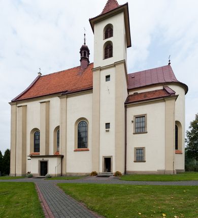 Zdjęcie nr 32: Kościół jest jednonawowy, trójprzęsłowy, z płytkimi kaplicami tworzącymi pseudotransept i jednoprzęsłowym prezbiterium zakończonym apsydą. Do prezbiterium przylegają dwa aneksy mieszące w przyziemiu zakrystię i skarbczyk, a na piętrze empory otwarte na prezbiterium. Do nawy od południa dostawiona jest kruchta. W naroża między kaplicami a nawą wstawiono dwie wieże-dzwonnice z klatkami schodowymi prowadzącymi na empory. Nawa jest rozczłonkowana płaskimi, szerokimi pilastrami toskańskimi, a nakryta sklepieniem kolebkowym z lunetami; prezbiterium przykryte sklepieniem kolebkowym z żebrami spływającymi na wsporniki, apsyda sklepieniem parasolowatym.  Prezbiterium ujęte dwiema głębokimi, półkoliście zamkniętymi wnękami, nad którymi parapety empor z ślepymi arkadkami z balasów jenolalkowych i łuków półkolistych. Wnętrze oświetlają wysokie i szerokie okna zamknięte półkoliście. W aneksach przy prezbiterium i w emporach znajdują się okna prostokątne. Fasada dwustrefowa, trójosiowa, ale osie i strefy wyznaczone jedynie przez okna, drzwi i nisze, zamknięta trójkątnie.    
Portal prostokątnych drzwi utworzony z pary żłobkowanych, toskańskich pilastrów, podtrzymujących belkowanie z trójkątnym przyczółkiem. Fryz belkowania ozdobiony tryglifami z łezkami i metopami w kształcie rozet i talerzy, a przyczółek kostkowaniem. Nad portalem okno w głębokim rozglifieniu, w kształcie prostokąta zamkniętego półkoliście. Po bokach portalu i okna głębokie nisze ujęte od dołu i góry odcinkami gzymsu. Zewnętrzne elewacje ujęte częściowo szkarpami, częściowo lizenami. W wieżach wejścia do kościoła i na klatki schodowe oraz niewielkie okienka w klatce schodowej i prześwity zamknięte półkoliście w dzwonnicach. Dachy dwuspadowe, na wieżach czterospadowe, nad nawą, wieżami i aneksami przy prezbiterium kryte dachówką, nad prezbiterium blachą. Na dachu wieżyczka na sygnaturkę. 
