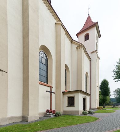 Zdjęcie nr 33: Kościół jest jednonawowy, trójprzęsłowy, z płytkimi kaplicami tworzącymi pseudotransept i jednoprzęsłowym prezbiterium zakończonym apsydą. Do prezbiterium przylegają dwa aneksy mieszące w przyziemiu zakrystię i skarbczyk, a na piętrze empory otwarte na prezbiterium. Do nawy od południa dostawiona jest kruchta. W naroża między kaplicami a nawą wstawiono dwie wieże-dzwonnice z klatkami schodowymi prowadzącymi na empory. Nawa jest rozczłonkowana płaskimi, szerokimi pilastrami toskańskimi, a nakryta sklepieniem kolebkowym z lunetami; prezbiterium przykryte sklepieniem kolebkowym z żebrami spływającymi na wsporniki, apsyda sklepieniem parasolowatym.  Prezbiterium ujęte dwiema głębokimi, półkoliście zamkniętymi wnękami, nad którymi parapety empor z ślepymi arkadkami z balasów jenolalkowych i łuków półkolistych. Wnętrze oświetlają wysokie i szerokie okna zamknięte półkoliście. W aneksach przy prezbiterium i w emporach znajdują się okna prostokątne. Fasada dwustrefowa, trójosiowa, ale osie i strefy wyznaczone jedynie przez okna, drzwi i nisze, zamknięta trójkątnie.    
Portal prostokątnych drzwi utworzony z pary żłobkowanych, toskańskich pilastrów, podtrzymujących belkowanie z trójkątnym przyczółkiem. Fryz belkowania ozdobiony tryglifami z łezkami i metopami w kształcie rozet i talerzy, a przyczółek kostkowaniem. Nad portalem okno w głębokim rozglifieniu, w kształcie prostokąta zamkniętego półkoliście. Po bokach portalu i okna głębokie nisze ujęte od dołu i góry odcinkami gzymsu. Zewnętrzne elewacje ujęte częściowo szkarpami, częściowo lizenami. W wieżach wejścia do kościoła i na klatki schodowe oraz niewielkie okienka w klatce schodowej i prześwity zamknięte półkoliście w dzwonnicach. Dachy dwuspadowe, na wieżach czterospadowe, nad nawą, wieżami i aneksami przy prezbiterium kryte dachówką, nad prezbiterium blachą. Na dachu wieżyczka na sygnaturkę. 
