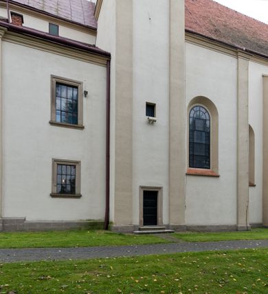 Zdjęcie nr 2: Kościół jest jednonawowy, trójprzęsłowy, z płytkimi kaplicami tworzącymi pseudotransept i jednoprzęsłowym prezbiterium zakończonym apsydą. Do prezbiterium przylegają dwa aneksy mieszące w przyziemiu zakrystię i skarbczyk, a na piętrze empory otwarte na prezbiterium. Do nawy od południa dostawiona jest kruchta. W naroża między kaplicami a nawą wstawiono dwie wieże-dzwonnice z klatkami schodowymi prowadzącymi na empory. Nawa jest rozczłonkowana płaskimi, szerokimi pilastrami toskańskimi, a nakryta sklepieniem kolebkowym z lunetami; prezbiterium przykryte sklepieniem kolebkowym z żebrami spływającymi na wsporniki, apsyda sklepieniem parasolowatym.  Prezbiterium ujęte dwiema głębokimi, półkoliście zamkniętymi wnękami, nad którymi parapety empor z ślepymi arkadkami z balasów jenolalkowych i łuków półkolistych. Wnętrze oświetlają wysokie i szerokie okna zamknięte półkoliście. W aneksach przy prezbiterium i w emporach znajdują się okna prostokątne. Fasada dwustrefowa, trójosiowa, ale osie i strefy wyznaczone jedynie przez okna, drzwi i nisze, zamknięta trójkątnie.    
Portal prostokątnych drzwi utworzony z pary żłobkowanych, toskańskich pilastrów, podtrzymujących belkowanie z trójkątnym przyczółkiem. Fryz belkowania ozdobiony tryglifami z łezkami i metopami w kształcie rozet i talerzy, a przyczółek kostkowaniem. Nad portalem okno w głębokim rozglifieniu, w kształcie prostokąta zamkniętego półkoliście. Po bokach portalu i okna głębokie nisze ujęte od dołu i góry odcinkami gzymsu. Zewnętrzne elewacje ujęte częściowo szkarpami, częściowo lizenami. W wieżach wejścia do kościoła i na klatki schodowe oraz niewielkie okienka w klatce schodowej i prześwity zamknięte półkoliście w dzwonnicach. Dachy dwuspadowe, na wieżach czterospadowe, nad nawą, wieżami i aneksami przy prezbiterium kryte dachówką, nad prezbiterium blachą. Na dachu wieżyczka na sygnaturkę. 
