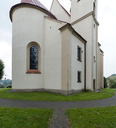 Zdjęcie nr 5: Kościół jest jednonawowy, trójprzęsłowy, z płytkimi kaplicami tworzącymi pseudotransept i jednoprzęsłowym prezbiterium zakończonym apsydą. Do prezbiterium przylegają dwa aneksy mieszące w przyziemiu zakrystię i skarbczyk, a na piętrze empory otwarte na prezbiterium. Do nawy od południa dostawiona jest kruchta. W naroża między kaplicami a nawą wstawiono dwie wieże-dzwonnice z klatkami schodowymi prowadzącymi na empory. Nawa jest rozczłonkowana płaskimi, szerokimi pilastrami toskańskimi, a nakryta sklepieniem kolebkowym z lunetami; prezbiterium przykryte sklepieniem kolebkowym z żebrami spływającymi na wsporniki, apsyda sklepieniem parasolowatym.  Prezbiterium ujęte dwiema głębokimi, półkoliście zamkniętymi wnękami, nad którymi parapety empor z ślepymi arkadkami z balasów jenolalkowych i łuków półkolistych. Wnętrze oświetlają wysokie i szerokie okna zamknięte półkoliście. W aneksach przy prezbiterium i w emporach znajdują się okna prostokątne. Fasada dwustrefowa, trójosiowa, ale osie i strefy wyznaczone jedynie przez okna, drzwi i nisze, zamknięta trójkątnie.    
Portal prostokątnych drzwi utworzony z pary żłobkowanych, toskańskich pilastrów, podtrzymujących belkowanie z trójkątnym przyczółkiem. Fryz belkowania ozdobiony tryglifami z łezkami i metopami w kształcie rozet i talerzy, a przyczółek kostkowaniem. Nad portalem okno w głębokim rozglifieniu, w kształcie prostokąta zamkniętego półkoliście. Po bokach portalu i okna głębokie nisze ujęte od dołu i góry odcinkami gzymsu. Zewnętrzne elewacje ujęte częściowo szkarpami, częściowo lizenami. W wieżach wejścia do kościoła i na klatki schodowe oraz niewielkie okienka w klatce schodowej i prześwity zamknięte półkoliście w dzwonnicach. Dachy dwuspadowe, na wieżach czterospadowe, nad nawą, wieżami i aneksami przy prezbiterium kryte dachówką, nad prezbiterium blachą. Na dachu wieżyczka na sygnaturkę. 
