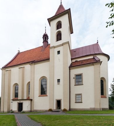 Zdjęcie nr 27: Kościół jest jednonawowy, trójprzęsłowy, z płytkimi kaplicami tworzącymi pseudotransept i jednoprzęsłowym prezbiterium zakończonym apsydą. Do prezbiterium przylegają dwa aneksy mieszące w przyziemiu zakrystię i skarbczyk, a na piętrze empory otwarte na prezbiterium. Do nawy od południa dostawiona jest kruchta. W naroża między kaplicami a nawą wstawiono dwie wieże-dzwonnice z klatkami schodowymi prowadzącymi na empory. Nawa jest rozczłonkowana płaskimi, szerokimi pilastrami toskańskimi, a nakryta sklepieniem kolebkowym z lunetami; prezbiterium przykryte sklepieniem kolebkowym z żebrami spływającymi na wsporniki, apsyda sklepieniem parasolowatym.  Prezbiterium ujęte dwiema głębokimi, półkoliście zamkniętymi wnękami, nad którymi parapety empor z ślepymi arkadkami z balasów jenolalkowych i łuków półkolistych. Wnętrze oświetlają wysokie i szerokie okna zamknięte półkoliście. W aneksach przy prezbiterium i w emporach znajdują się okna prostokątne. Fasada dwustrefowa, trójosiowa, ale osie i strefy wyznaczone jedynie przez okna, drzwi i nisze, zamknięta trójkątnie.    
Portal prostokątnych drzwi utworzony z pary żłobkowanych, toskańskich pilastrów, podtrzymujących belkowanie z trójkątnym przyczółkiem. Fryz belkowania ozdobiony tryglifami z łezkami i metopami w kształcie rozet i talerzy, a przyczółek kostkowaniem. Nad portalem okno w głębokim rozglifieniu, w kształcie prostokąta zamkniętego półkoliście. Po bokach portalu i okna głębokie nisze ujęte od dołu i góry odcinkami gzymsu. Zewnętrzne elewacje ujęte częściowo szkarpami, częściowo lizenami. W wieżach wejścia do kościoła i na klatki schodowe oraz niewielkie okienka w klatce schodowej i prześwity zamknięte półkoliście w dzwonnicach. Dachy dwuspadowe, na wieżach czterospadowe, nad nawą, wieżami i aneksami przy prezbiterium kryte dachówką, nad prezbiterium blachą. Na dachu wieżyczka na sygnaturkę. 

