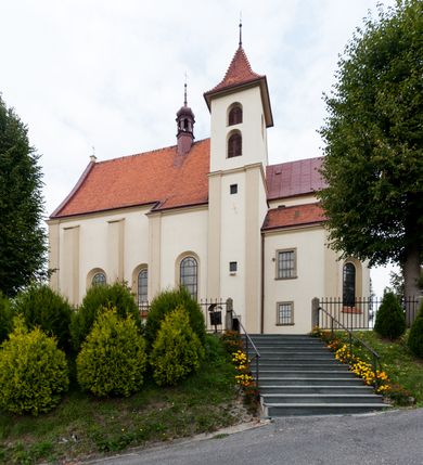 Zdjęcie nr 8: Kościół jest jednonawowy, trójprzęsłowy, z płytkimi kaplicami tworzącymi pseudotransept i jednoprzęsłowym prezbiterium zakończonym apsydą. Do prezbiterium przylegają dwa aneksy mieszące w przyziemiu zakrystię i skarbczyk, a na piętrze empory otwarte na prezbiterium. Do nawy od południa dostawiona jest kruchta. W naroża między kaplicami a nawą wstawiono dwie wieże-dzwonnice z klatkami schodowymi prowadzącymi na empory. Nawa jest rozczłonkowana płaskimi, szerokimi pilastrami toskańskimi, a nakryta sklepieniem kolebkowym z lunetami; prezbiterium przykryte sklepieniem kolebkowym z żebrami spływającymi na wsporniki, apsyda sklepieniem parasolowatym.  Prezbiterium ujęte dwiema głębokimi, półkoliście zamkniętymi wnękami, nad którymi parapety empor z ślepymi arkadkami z balasów jenolalkowych i łuków półkolistych. Wnętrze oświetlają wysokie i szerokie okna zamknięte półkoliście. W aneksach przy prezbiterium i w emporach znajdują się okna prostokątne. Fasada dwustrefowa, trójosiowa, ale osie i strefy wyznaczone jedynie przez okna, drzwi i nisze, zamknięta trójkątnie.    
Portal prostokątnych drzwi utworzony z pary żłobkowanych, toskańskich pilastrów, podtrzymujących belkowanie z trójkątnym przyczółkiem. Fryz belkowania ozdobiony tryglifami z łezkami i metopami w kształcie rozet i talerzy, a przyczółek kostkowaniem. Nad portalem okno w głębokim rozglifieniu, w kształcie prostokąta zamkniętego półkoliście. Po bokach portalu i okna głębokie nisze ujęte od dołu i góry odcinkami gzymsu. Zewnętrzne elewacje ujęte częściowo szkarpami, częściowo lizenami. W wieżach wejścia do kościoła i na klatki schodowe oraz niewielkie okienka w klatce schodowej i prześwity zamknięte półkoliście w dzwonnicach. Dachy dwuspadowe, na wieżach czterospadowe, nad nawą, wieżami i aneksami przy prezbiterium kryte dachówką, nad prezbiterium blachą. Na dachu wieżyczka na sygnaturkę. 
