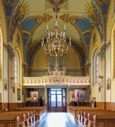 Zdjęcie nr 16: Kościół jest jednonawowy, trójprzęsłowy, z płytkimi kaplicami tworzącymi pseudotransept i jednoprzęsłowym prezbiterium zakończonym apsydą. Do prezbiterium przylegają dwa aneksy mieszące w przyziemiu zakrystię i skarbczyk, a na piętrze empory otwarte na prezbiterium. Do nawy od południa dostawiona jest kruchta. W naroża między kaplicami a nawą wstawiono dwie wieże-dzwonnice z klatkami schodowymi prowadzącymi na empory. Nawa jest rozczłonkowana płaskimi, szerokimi pilastrami toskańskimi, a nakryta sklepieniem kolebkowym z lunetami; prezbiterium przykryte sklepieniem kolebkowym z żebrami spływającymi na wsporniki, apsyda sklepieniem parasolowatym.  Prezbiterium ujęte dwiema głębokimi, półkoliście zamkniętymi wnękami, nad którymi parapety empor z ślepymi arkadkami z balasów jenolalkowych i łuków półkolistych. Wnętrze oświetlają wysokie i szerokie okna zamknięte półkoliście. W aneksach przy prezbiterium i w emporach znajdują się okna prostokątne. Fasada dwustrefowa, trójosiowa, ale osie i strefy wyznaczone jedynie przez okna, drzwi i nisze, zamknięta trójkątnie.    
Portal prostokątnych drzwi utworzony z pary żłobkowanych, toskańskich pilastrów, podtrzymujących belkowanie z trójkątnym przyczółkiem. Fryz belkowania ozdobiony tryglifami z łezkami i metopami w kształcie rozet i talerzy, a przyczółek kostkowaniem. Nad portalem okno w głębokim rozglifieniu, w kształcie prostokąta zamkniętego półkoliście. Po bokach portalu i okna głębokie nisze ujęte od dołu i góry odcinkami gzymsu. Zewnętrzne elewacje ujęte częściowo szkarpami, częściowo lizenami. W wieżach wejścia do kościoła i na klatki schodowe oraz niewielkie okienka w klatce schodowej i prześwity zamknięte półkoliście w dzwonnicach. Dachy dwuspadowe, na wieżach czterospadowe, nad nawą, wieżami i aneksami przy prezbiterium kryte dachówką, nad prezbiterium blachą. Na dachu wieżyczka na sygnaturkę. 
