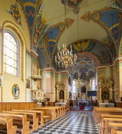 Zdjęcie nr 15: Kościół jest jednonawowy, trójprzęsłowy, z płytkimi kaplicami tworzącymi pseudotransept i jednoprzęsłowym prezbiterium zakończonym apsydą. Do prezbiterium przylegają dwa aneksy mieszące w przyziemiu zakrystię i skarbczyk, a na piętrze empory otwarte na prezbiterium. Do nawy od południa dostawiona jest kruchta. W naroża między kaplicami a nawą wstawiono dwie wieże-dzwonnice z klatkami schodowymi prowadzącymi na empory. Nawa jest rozczłonkowana płaskimi, szerokimi pilastrami toskańskimi, a nakryta sklepieniem kolebkowym z lunetami; prezbiterium przykryte sklepieniem kolebkowym z żebrami spływającymi na wsporniki, apsyda sklepieniem parasolowatym.  Prezbiterium ujęte dwiema głębokimi, półkoliście zamkniętymi wnękami, nad którymi parapety empor z ślepymi arkadkami z balasów jenolalkowych i łuków półkolistych. Wnętrze oświetlają wysokie i szerokie okna zamknięte półkoliście. W aneksach przy prezbiterium i w emporach znajdują się okna prostokątne. Fasada dwustrefowa, trójosiowa, ale osie i strefy wyznaczone jedynie przez okna, drzwi i nisze, zamknięta trójkątnie.    
Portal prostokątnych drzwi utworzony z pary żłobkowanych, toskańskich pilastrów, podtrzymujących belkowanie z trójkątnym przyczółkiem. Fryz belkowania ozdobiony tryglifami z łezkami i metopami w kształcie rozet i talerzy, a przyczółek kostkowaniem. Nad portalem okno w głębokim rozglifieniu, w kształcie prostokąta zamkniętego półkoliście. Po bokach portalu i okna głębokie nisze ujęte od dołu i góry odcinkami gzymsu. Zewnętrzne elewacje ujęte częściowo szkarpami, częściowo lizenami. W wieżach wejścia do kościoła i na klatki schodowe oraz niewielkie okienka w klatce schodowej i prześwity zamknięte półkoliście w dzwonnicach. Dachy dwuspadowe, na wieżach czterospadowe, nad nawą, wieżami i aneksami przy prezbiterium kryte dachówką, nad prezbiterium blachą. Na dachu wieżyczka na sygnaturkę. 
