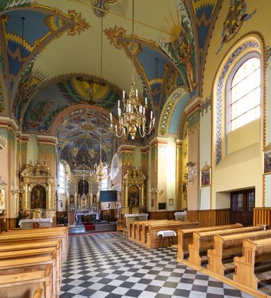 Zdjęcie nr 11: Kościół jest jednonawowy, trójprzęsłowy, z płytkimi kaplicami tworzącymi pseudotransept i jednoprzęsłowym prezbiterium zakończonym apsydą. Do prezbiterium przylegają dwa aneksy mieszące w przyziemiu zakrystię i skarbczyk, a na piętrze empory otwarte na prezbiterium. Do nawy od południa dostawiona jest kruchta. W naroża między kaplicami a nawą wstawiono dwie wieże-dzwonnice z klatkami schodowymi prowadzącymi na empory. Nawa jest rozczłonkowana płaskimi, szerokimi pilastrami toskańskimi, a nakryta sklepieniem kolebkowym z lunetami; prezbiterium przykryte sklepieniem kolebkowym z żebrami spływającymi na wsporniki, apsyda sklepieniem parasolowatym.  Prezbiterium ujęte dwiema głębokimi, półkoliście zamkniętymi wnękami, nad którymi parapety empor z ślepymi arkadkami z balasów jenolalkowych i łuków półkolistych. Wnętrze oświetlają wysokie i szerokie okna zamknięte półkoliście. W aneksach przy prezbiterium i w emporach znajdują się okna prostokątne. Fasada dwustrefowa, trójosiowa, ale osie i strefy wyznaczone jedynie przez okna, drzwi i nisze, zamknięta trójkątnie.    
Portal prostokątnych drzwi utworzony z pary żłobkowanych, toskańskich pilastrów, podtrzymujących belkowanie z trójkątnym przyczółkiem. Fryz belkowania ozdobiony tryglifami z łezkami i metopami w kształcie rozet i talerzy, a przyczółek kostkowaniem. Nad portalem okno w głębokim rozglifieniu, w kształcie prostokąta zamkniętego półkoliście. Po bokach portalu i okna głębokie nisze ujęte od dołu i góry odcinkami gzymsu. Zewnętrzne elewacje ujęte częściowo szkarpami, częściowo lizenami. W wieżach wejścia do kościoła i na klatki schodowe oraz niewielkie okienka w klatce schodowej i prześwity zamknięte półkoliście w dzwonnicach. Dachy dwuspadowe, na wieżach czterospadowe, nad nawą, wieżami i aneksami przy prezbiterium kryte dachówką, nad prezbiterium blachą. Na dachu wieżyczka na sygnaturkę. 
