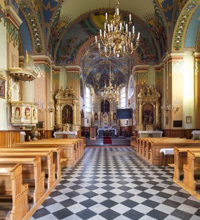 Zdjęcie nr 10: Kościół jest jednonawowy, trójprzęsłowy, z płytkimi kaplicami tworzącymi pseudotransept i jednoprzęsłowym prezbiterium zakończonym apsydą. Do prezbiterium przylegają dwa aneksy mieszące w przyziemiu zakrystię i skarbczyk, a na piętrze empory otwarte na prezbiterium. Do nawy od południa dostawiona jest kruchta. W naroża między kaplicami a nawą wstawiono dwie wieże-dzwonnice z klatkami schodowymi prowadzącymi na empory. Nawa jest rozczłonkowana płaskimi, szerokimi pilastrami toskańskimi, a nakryta sklepieniem kolebkowym z lunetami; prezbiterium przykryte sklepieniem kolebkowym z żebrami spływającymi na wsporniki, apsyda sklepieniem parasolowatym.  Prezbiterium ujęte dwiema głębokimi, półkoliście zamkniętymi wnękami, nad którymi parapety empor z ślepymi arkadkami z balasów jenolalkowych i łuków półkolistych. Wnętrze oświetlają wysokie i szerokie okna zamknięte półkoliście. W aneksach przy prezbiterium i w emporach znajdują się okna prostokątne. Fasada dwustrefowa, trójosiowa, ale osie i strefy wyznaczone jedynie przez okna, drzwi i nisze, zamknięta trójkątnie.    
Portal prostokątnych drzwi utworzony z pary żłobkowanych, toskańskich pilastrów, podtrzymujących belkowanie z trójkątnym przyczółkiem. Fryz belkowania ozdobiony tryglifami z łezkami i metopami w kształcie rozet i talerzy, a przyczółek kostkowaniem. Nad portalem okno w głębokim rozglifieniu, w kształcie prostokąta zamkniętego półkoliście. Po bokach portalu i okna głębokie nisze ujęte od dołu i góry odcinkami gzymsu. Zewnętrzne elewacje ujęte częściowo szkarpami, częściowo lizenami. W wieżach wejścia do kościoła i na klatki schodowe oraz niewielkie okienka w klatce schodowej i prześwity zamknięte półkoliście w dzwonnicach. Dachy dwuspadowe, na wieżach czterospadowe, nad nawą, wieżami i aneksami przy prezbiterium kryte dachówką, nad prezbiterium blachą. Na dachu wieżyczka na sygnaturkę. 
