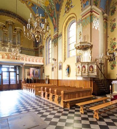 Zdjęcie nr 13: Kościół jest jednonawowy, trójprzęsłowy, z płytkimi kaplicami tworzącymi pseudotransept i jednoprzęsłowym prezbiterium zakończonym apsydą. Do prezbiterium przylegają dwa aneksy mieszące w przyziemiu zakrystię i skarbczyk, a na piętrze empory otwarte na prezbiterium. Do nawy od południa dostawiona jest kruchta. W naroża między kaplicami a nawą wstawiono dwie wieże-dzwonnice z klatkami schodowymi prowadzącymi na empory. Nawa jest rozczłonkowana płaskimi, szerokimi pilastrami toskańskimi, a nakryta sklepieniem kolebkowym z lunetami; prezbiterium przykryte sklepieniem kolebkowym z żebrami spływającymi na wsporniki, apsyda sklepieniem parasolowatym.  Prezbiterium ujęte dwiema głębokimi, półkoliście zamkniętymi wnękami, nad którymi parapety empor z ślepymi arkadkami z balasów jenolalkowych i łuków półkolistych. Wnętrze oświetlają wysokie i szerokie okna zamknięte półkoliście. W aneksach przy prezbiterium i w emporach znajdują się okna prostokątne. Fasada dwustrefowa, trójosiowa, ale osie i strefy wyznaczone jedynie przez okna, drzwi i nisze, zamknięta trójkątnie.    
Portal prostokątnych drzwi utworzony z pary żłobkowanych, toskańskich pilastrów, podtrzymujących belkowanie z trójkątnym przyczółkiem. Fryz belkowania ozdobiony tryglifami z łezkami i metopami w kształcie rozet i talerzy, a przyczółek kostkowaniem. Nad portalem okno w głębokim rozglifieniu, w kształcie prostokąta zamkniętego półkoliście. Po bokach portalu i okna głębokie nisze ujęte od dołu i góry odcinkami gzymsu. Zewnętrzne elewacje ujęte częściowo szkarpami, częściowo lizenami. W wieżach wejścia do kościoła i na klatki schodowe oraz niewielkie okienka w klatce schodowej i prześwity zamknięte półkoliście w dzwonnicach. Dachy dwuspadowe, na wieżach czterospadowe, nad nawą, wieżami i aneksami przy prezbiterium kryte dachówką, nad prezbiterium blachą. Na dachu wieżyczka na sygnaturkę. 
