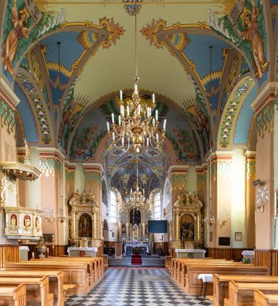 Zdjęcie nr 14: Kościół jest jednonawowy, trójprzęsłowy, z płytkimi kaplicami tworzącymi pseudotransept i jednoprzęsłowym prezbiterium zakończonym apsydą. Do prezbiterium przylegają dwa aneksy mieszące w przyziemiu zakrystię i skarbczyk, a na piętrze empory otwarte na prezbiterium. Do nawy od południa dostawiona jest kruchta. W naroża między kaplicami a nawą wstawiono dwie wieże-dzwonnice z klatkami schodowymi prowadzącymi na empory. Nawa jest rozczłonkowana płaskimi, szerokimi pilastrami toskańskimi, a nakryta sklepieniem kolebkowym z lunetami; prezbiterium przykryte sklepieniem kolebkowym z żebrami spływającymi na wsporniki, apsyda sklepieniem parasolowatym.  Prezbiterium ujęte dwiema głębokimi, półkoliście zamkniętymi wnękami, nad którymi parapety empor z ślepymi arkadkami z balasów jenolalkowych i łuków półkolistych. Wnętrze oświetlają wysokie i szerokie okna zamknięte półkoliście. W aneksach przy prezbiterium i w emporach znajdują się okna prostokątne. Fasada dwustrefowa, trójosiowa, ale osie i strefy wyznaczone jedynie przez okna, drzwi i nisze, zamknięta trójkątnie.    
Portal prostokątnych drzwi utworzony z pary żłobkowanych, toskańskich pilastrów, podtrzymujących belkowanie z trójkątnym przyczółkiem. Fryz belkowania ozdobiony tryglifami z łezkami i metopami w kształcie rozet i talerzy, a przyczółek kostkowaniem. Nad portalem okno w głębokim rozglifieniu, w kształcie prostokąta zamkniętego półkoliście. Po bokach portalu i okna głębokie nisze ujęte od dołu i góry odcinkami gzymsu. Zewnętrzne elewacje ujęte częściowo szkarpami, częściowo lizenami. W wieżach wejścia do kościoła i na klatki schodowe oraz niewielkie okienka w klatce schodowej i prześwity zamknięte półkoliście w dzwonnicach. Dachy dwuspadowe, na wieżach czterospadowe, nad nawą, wieżami i aneksami przy prezbiterium kryte dachówką, nad prezbiterium blachą. Na dachu wieżyczka na sygnaturkę. 
