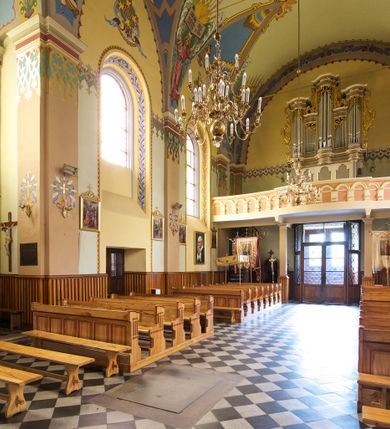 Zdjęcie nr 20: Kościół jest jednonawowy, trójprzęsłowy, z płytkimi kaplicami tworzącymi pseudotransept i jednoprzęsłowym prezbiterium zakończonym apsydą. Do prezbiterium przylegają dwa aneksy mieszące w przyziemiu zakrystię i skarbczyk, a na piętrze empory otwarte na prezbiterium. Do nawy od południa dostawiona jest kruchta. W naroża między kaplicami a nawą wstawiono dwie wieże-dzwonnice z klatkami schodowymi prowadzącymi na empory. Nawa jest rozczłonkowana płaskimi, szerokimi pilastrami toskańskimi, a nakryta sklepieniem kolebkowym z lunetami; prezbiterium przykryte sklepieniem kolebkowym z żebrami spływającymi na wsporniki, apsyda sklepieniem parasolowatym.  Prezbiterium ujęte dwiema głębokimi, półkoliście zamkniętymi wnękami, nad którymi parapety empor z ślepymi arkadkami z balasów jenolalkowych i łuków półkolistych. Wnętrze oświetlają wysokie i szerokie okna zamknięte półkoliście. W aneksach przy prezbiterium i w emporach znajdują się okna prostokątne. Fasada dwustrefowa, trójosiowa, ale osie i strefy wyznaczone jedynie przez okna, drzwi i nisze, zamknięta trójkątnie.    
Portal prostokątnych drzwi utworzony z pary żłobkowanych, toskańskich pilastrów, podtrzymujących belkowanie z trójkątnym przyczółkiem. Fryz belkowania ozdobiony tryglifami z łezkami i metopami w kształcie rozet i talerzy, a przyczółek kostkowaniem. Nad portalem okno w głębokim rozglifieniu, w kształcie prostokąta zamkniętego półkoliście. Po bokach portalu i okna głębokie nisze ujęte od dołu i góry odcinkami gzymsu. Zewnętrzne elewacje ujęte częściowo szkarpami, częściowo lizenami. W wieżach wejścia do kościoła i na klatki schodowe oraz niewielkie okienka w klatce schodowej i prześwity zamknięte półkoliście w dzwonnicach. Dachy dwuspadowe, na wieżach czterospadowe, nad nawą, wieżami i aneksami przy prezbiterium kryte dachówką, nad prezbiterium blachą. Na dachu wieżyczka na sygnaturkę. 
