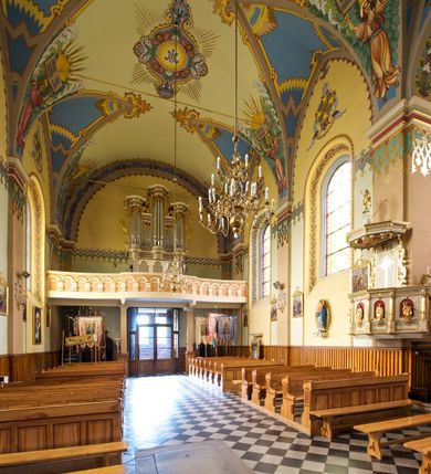 Zdjęcie nr 19: Kościół jest jednonawowy, trójprzęsłowy, z płytkimi kaplicami tworzącymi pseudotransept i jednoprzęsłowym prezbiterium zakończonym apsydą. Do prezbiterium przylegają dwa aneksy mieszące w przyziemiu zakrystię i skarbczyk, a na piętrze empory otwarte na prezbiterium. Do nawy od południa dostawiona jest kruchta. W naroża między kaplicami a nawą wstawiono dwie wieże-dzwonnice z klatkami schodowymi prowadzącymi na empory. Nawa jest rozczłonkowana płaskimi, szerokimi pilastrami toskańskimi, a nakryta sklepieniem kolebkowym z lunetami; prezbiterium przykryte sklepieniem kolebkowym z żebrami spływającymi na wsporniki, apsyda sklepieniem parasolowatym.  Prezbiterium ujęte dwiema głębokimi, półkoliście zamkniętymi wnękami, nad którymi parapety empor z ślepymi arkadkami z balasów jenolalkowych i łuków półkolistych. Wnętrze oświetlają wysokie i szerokie okna zamknięte półkoliście. W aneksach przy prezbiterium i w emporach znajdują się okna prostokątne. Fasada dwustrefowa, trójosiowa, ale osie i strefy wyznaczone jedynie przez okna, drzwi i nisze, zamknięta trójkątnie.    
Portal prostokątnych drzwi utworzony z pary żłobkowanych, toskańskich pilastrów, podtrzymujących belkowanie z trójkątnym przyczółkiem. Fryz belkowania ozdobiony tryglifami z łezkami i metopami w kształcie rozet i talerzy, a przyczółek kostkowaniem. Nad portalem okno w głębokim rozglifieniu, w kształcie prostokąta zamkniętego półkoliście. Po bokach portalu i okna głębokie nisze ujęte od dołu i góry odcinkami gzymsu. Zewnętrzne elewacje ujęte częściowo szkarpami, częściowo lizenami. W wieżach wejścia do kościoła i na klatki schodowe oraz niewielkie okienka w klatce schodowej i prześwity zamknięte półkoliście w dzwonnicach. Dachy dwuspadowe, na wieżach czterospadowe, nad nawą, wieżami i aneksami przy prezbiterium kryte dachówką, nad prezbiterium blachą. Na dachu wieżyczka na sygnaturkę. 
