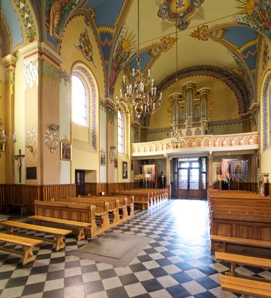 Zdjęcie nr 18: Kościół jest jednonawowy, trójprzęsłowy, z płytkimi kaplicami tworzącymi pseudotransept i jednoprzęsłowym prezbiterium zakończonym apsydą. Do prezbiterium przylegają dwa aneksy mieszące w przyziemiu zakrystię i skarbczyk, a na piętrze empory otwarte na prezbiterium. Do nawy od południa dostawiona jest kruchta. W naroża między kaplicami a nawą wstawiono dwie wieże-dzwonnice z klatkami schodowymi prowadzącymi na empory. Nawa jest rozczłonkowana płaskimi, szerokimi pilastrami toskańskimi, a nakryta sklepieniem kolebkowym z lunetami; prezbiterium przykryte sklepieniem kolebkowym z żebrami spływającymi na wsporniki, apsyda sklepieniem parasolowatym.  Prezbiterium ujęte dwiema głębokimi, półkoliście zamkniętymi wnękami, nad którymi parapety empor z ślepymi arkadkami z balasów jenolalkowych i łuków półkolistych. Wnętrze oświetlają wysokie i szerokie okna zamknięte półkoliście. W aneksach przy prezbiterium i w emporach znajdują się okna prostokątne. Fasada dwustrefowa, trójosiowa, ale osie i strefy wyznaczone jedynie przez okna, drzwi i nisze, zamknięta trójkątnie.    
Portal prostokątnych drzwi utworzony z pary żłobkowanych, toskańskich pilastrów, podtrzymujących belkowanie z trójkątnym przyczółkiem. Fryz belkowania ozdobiony tryglifami z łezkami i metopami w kształcie rozet i talerzy, a przyczółek kostkowaniem. Nad portalem okno w głębokim rozglifieniu, w kształcie prostokąta zamkniętego półkoliście. Po bokach portalu i okna głębokie nisze ujęte od dołu i góry odcinkami gzymsu. Zewnętrzne elewacje ujęte częściowo szkarpami, częściowo lizenami. W wieżach wejścia do kościoła i na klatki schodowe oraz niewielkie okienka w klatce schodowej i prześwity zamknięte półkoliście w dzwonnicach. Dachy dwuspadowe, na wieżach czterospadowe, nad nawą, wieżami i aneksami przy prezbiterium kryte dachówką, nad prezbiterium blachą. Na dachu wieżyczka na sygnaturkę. 
