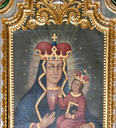 Zdjęcie nr 4: Obraz w kształcie stojącego prostokąta zamkniętego półkolistym łukiem nadwieszonym, uskokowym. Madonna w typie Hodegetrii została przedstawiona frontalnie, w półpostaci. Głowę ma lekko zwróconą w lewo, twarz owalną, o prostych rysach, jasnej karnacji, długim, wąskim nosie, dużych oczach w jasnej oprawie i drobnych ustach. Na prawym policzku dwa równoległe, ukośnie biegnące nacięcia. Maria ubrana jest w jasnoczerwoną suknię ze złoconym galonem pod szyją oraz dekorowany wzorami floralnymi ciemnoniebieski płaszcz ze złotą lamówką osłaniający głowę, ręce i korpus. Na szyi ma zawieszony podwójny sznur pereł ze złotym krzyżykiem, na głowie złotą koronę w typie otwartym, wysadzaną kamieniami szlachetnymi, z czerwonym wypełnieniem. Prawą ręką wskazuje na trzymane na lewej ręce siedzące Dzieciątko. Jezus jest zwrócony w trzech czwartych w prawo. Głowę ma lekko odchyloną na lewy bark, twarz owalną, o jasnej cerze i delikatnych rysach. Długie, brązowe, falowane włosy opadają mu na ramiona i plecy. Jest ubrany w czerwoną tunikę z wąskimi rękawami i złotymi obszyciami. Na głowie ma koronę w typie otwartym, wysadzaną szlachetnymi kamieniami z czerwonym wypełnieniem. Lewą ręką podtrzymuje księgę w oprawie ze złotym napisem IHS i zapięciami, prawą unosi w geście błogosławieństwa. Wokół głów postaci promieniste nimby i gwiazdki. Tło jednolite, szare. W górnej partii obrazu płaskorzeźbiony, ażurowy ornament stylizowanej wici roślinnej z okiem opatrzności Bożej w promienistej glorii pośrodku. Kolorystyka intensywna, mocne kontrasty kolorystyczne. Obraz ujęty złoconą, profilowaną ramą. 