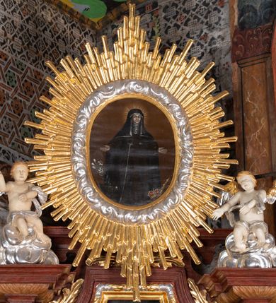 Zdjęcie nr 9: Ołtarz przyścienny, architektoniczny, jednokondygnacyjny, jednoosiowy, ze zwieńczeniem. Mensa w typie sarkofagowym z kamiennym portatylem, dekorowana w dolnej partii srebrnymi liśćmi akantu, a w górnej pośrodku płaskorzeźbiony monogram maryjny ujęty plakietami ornamentalnymi z kształtów nawiązujących do motywu rocaille’a; całość mensy groszkowana. Retabulum na cokole o wysuniętych bokach, ujęte parą kolumn o kapitelach akantowych i gładkich trzonach, wspierających fragmenty belkowania z silnie wysuniętymi fryzem i gzymsem. Pola cokołu retabulum zdobione motywem wici akantowej, z kartuszem w kształcie leżącego owalu pośrodku z ciemnoniebieskim napisem na jasnoniebieskim tle „POMŃIK od NOWIEŃA / OŁTARZA ZPOŻYCZKI HARKLOwy / dodał Utrzymańie przy tej Robocie Stanisław Plewa. / w. 1856”. Oś środkową nastawy wypełnia pole w kształcie stojącego prostokąta o wklęsłych górnych narożach, ujęte profilowaną, częściowo złoconą ramą, z motywem liści laurowych. W polu obraz z przedstawieniem Madonny z Dzieciątkiem. Kondygnację flankują ażurowe uszaki utworzone z bujnej, mięsistej wici akantu. Zwieńczenie tworzy owalne przedstawienie św. Kingi otoczone srebrnymi obłokami oraz glorią promienistą o promieniach różnej długości. Zwieńczenie flankuje para nagich aniołków posadowionych na srebrzonych chmurach, umieszczonych na fragmentach belkowania retabulum. 
Struktura polichromowana w kolorze brązowym. Partie detalu architektonicznego i ornamentyka złocone i srebrzone. 
