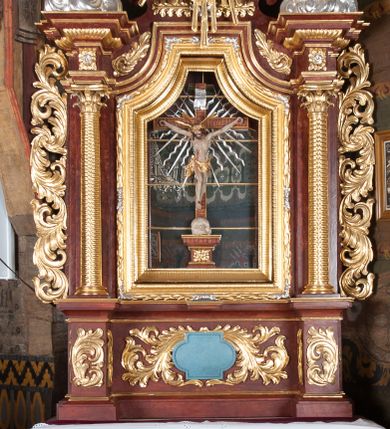 Zdjęcie nr 1: Ołtarz przyścienny, architektoniczny, jednokondygnacyjny, jednoosiowy, ze zwieńczeniem. Mensa w typie sarkofagowym z kamiennym portatylem, dekorowana w dolnej partii srebrnymi liśćmi akantu, a w górnej plakietą w kształcie leżącego prostokąta o zaokrąglonych narożach przenikającego owal; kształt wypełniają odchodzące od centralnego pola złote promienie. Ujmują je plakiety ornamentalne z kształtów nawiązujących do motywu rocaille’a; całość mensy groszkowana. Retabulum na cokole o wysuniętych bokach, ujęte parą kolumn o kapitelach akantowych i trzonach zdobionych żłobkowaniem od frontu, wspierających fragmenty belkowania z silnie wysuniętymi fryzem i gzymsem. Pola cokołu retabulum zdobione motywem wici akantowej ujmującej jasnoniebieski kartusz w kształcie leżącego owalu przenikającego się ze stojącym prostokątem. Oś środkową nastawy wypełnia pole w kształcie stojącego prostokąta o wklęsłych górnych narożach, ujęte profilowaną, częściowo złoconą ramą, z motywem liści laurowych. W środku wizerunek ukrzyżowanego Jezusa na tle lustra. Na zasuwie obraz św. Teresy od Dzieciątka Jezus. Kondygnację flankują ażurowe uszaki utworzone z bujnej, mięsistej wici z liści akantu. Zwieńczenie tworzy owalne przedstawienie św. Antoniego Padewskiego otoczone srebrnymi obłokami oraz glorią promienistą o promieniach różnej długości. Zwieńczenie flankuje para nagich aniołków posadowionych na srebrzonych chmurach, umieszczonych na fragmentach belkowania retabulum. 
Struktura polichromowana w kolorze brązowym. Partie detalu architektonicznego i ornamentyka złocone i srebrzone. 
