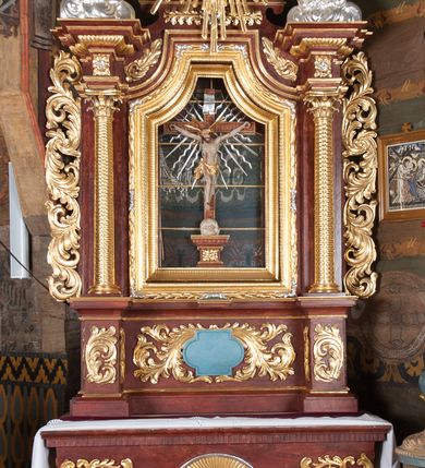 Zdjęcie nr 2: Ołtarz przyścienny, architektoniczny, jednokondygnacyjny, jednoosiowy, ze zwieńczeniem. Mensa w typie sarkofagowym z kamiennym portatylem, dekorowana w dolnej partii srebrnymi liśćmi akantu, a w górnej plakietą w kształcie leżącego prostokąta o zaokrąglonych narożach przenikającego owal; kształt wypełniają odchodzące od centralnego pola złote promienie. Ujmują je plakiety ornamentalne z kształtów nawiązujących do motywu rocaille’a; całość mensy groszkowana. Retabulum na cokole o wysuniętych bokach, ujęte parą kolumn o kapitelach akantowych i trzonach zdobionych żłobkowaniem od frontu, wspierających fragmenty belkowania z silnie wysuniętymi fryzem i gzymsem. Pola cokołu retabulum zdobione motywem wici akantowej ujmującej jasnoniebieski kartusz w kształcie leżącego owalu przenikającego się ze stojącym prostokątem. Oś środkową nastawy wypełnia pole w kształcie stojącego prostokąta o wklęsłych górnych narożach, ujęte profilowaną, częściowo złoconą ramą, z motywem liści laurowych. W środku wizerunek ukrzyżowanego Jezusa na tle lustra. Na zasuwie obraz św. Teresy od Dzieciątka Jezus. Kondygnację flankują ażurowe uszaki utworzone z bujnej, mięsistej wici z liści akantu. Zwieńczenie tworzy owalne przedstawienie św. Antoniego Padewskiego otoczone srebrnymi obłokami oraz glorią promienistą o promieniach różnej długości. Zwieńczenie flankuje para nagich aniołków posadowionych na srebrzonych chmurach, umieszczonych na fragmentach belkowania retabulum. 
Struktura polichromowana w kolorze brązowym. Partie detalu architektonicznego i ornamentyka złocone i srebrzone. 

