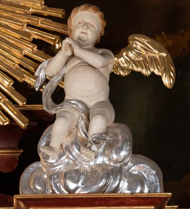 Zdjęcie nr 5: Ołtarz przyścienny, architektoniczny, jednokondygnacyjny, jednoosiowy, ze zwieńczeniem. Mensa w typie sarkofagowym z kamiennym portatylem, dekorowana w dolnej partii srebrnymi liśćmi akantu, a w górnej plakietą w kształcie leżącego prostokąta o zaokrąglonych narożach przenikającego owal; kształt wypełniają odchodzące od centralnego pola złote promienie. Ujmują je plakiety ornamentalne z kształtów nawiązujących do motywu rocaille’a; całość mensy groszkowana. Retabulum na cokole o wysuniętych bokach, ujęte parą kolumn o kapitelach akantowych i trzonach zdobionych żłobkowaniem od frontu, wspierających fragmenty belkowania z silnie wysuniętymi fryzem i gzymsem. Pola cokołu retabulum zdobione motywem wici akantowej ujmującej jasnoniebieski kartusz w kształcie leżącego owalu przenikającego się ze stojącym prostokątem. Oś środkową nastawy wypełnia pole w kształcie stojącego prostokąta o wklęsłych górnych narożach, ujęte profilowaną, częściowo złoconą ramą, z motywem liści laurowych. W środku wizerunek ukrzyżowanego Jezusa na tle lustra. Na zasuwie obraz św. Teresy od Dzieciątka Jezus. Kondygnację flankują ażurowe uszaki utworzone z bujnej, mięsistej wici z liści akantu. Zwieńczenie tworzy owalne przedstawienie św. Antoniego Padewskiego otoczone srebrnymi obłokami oraz glorią promienistą o promieniach różnej długości. Zwieńczenie flankuje para nagich aniołków posadowionych na srebrzonych chmurach, umieszczonych na fragmentach belkowania retabulum. 
Struktura polichromowana w kolorze brązowym. Partie detalu architektonicznego i ornamentyka złocone i srebrzone. 
