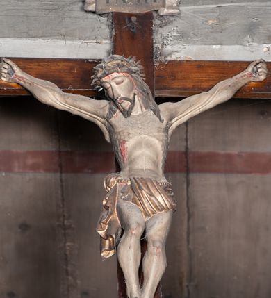 Zdjęcie nr 4: Chrystus rozpięty na krzyżu z szeroko rozłożonymi rękami, w lekkim zwisie ciała, z lekko ugiętymi kolanami i stopami założonymi prawa na lewą, przybitymi jednym gwoździem. Głowa pochylona na prawy bark. Twarz pociągła z długim nosem i wydatnymi kośćmi policzkowymi, okolona długimi ciemnymi włosami i zarostem. Ciało muskularne o ciemnej karnacji z zaznaczonymi śladami męki. Wokół bioder złocone perizonium podtrzymywane sznurem, ze zwisem draperii wzdłuż prawego uda. Matka Boska Bolesna ukazana w całej postaci, w ujęciu w trzech czwartych, zwrócona w lewo w kierunku krzyża; stoi w kontrapoście z głową przechyloną w lewo. Ręce ugięte w łokciach, dłonie skrzyżowane w przegubach ułożone na wysokości piersi. Ubrana w długą fałdzistą czerwoną suknię i narzucony na ramiona ciemnoniebieski płaszcz. Na głowie i ramionach biała chusta; wokół głowy nimb. Św. Jan Ewangelista przedstawiony w całej postaci, w ujęciu w trzech czwartych, zwrócony w prawo w kierunku krzyża.  Twarz o młodzieńczych rysach (bez zarostu), widoczna z profilu, zwrócona ku górze, ku Chrystusowi. Ręce ugięte w łokciach, z dłońmi złożonymi na piersiach na różnej wysokości. Ubrany w długą ciemnoniebieską suknię i czerwony płaszcz. Wokół głowy nimb.   